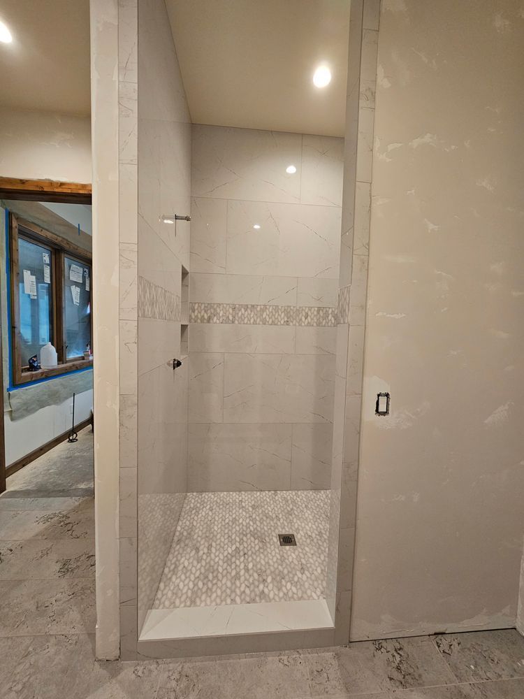 Completed shower with gray tile walls, mosaic floor, and glass door frame.