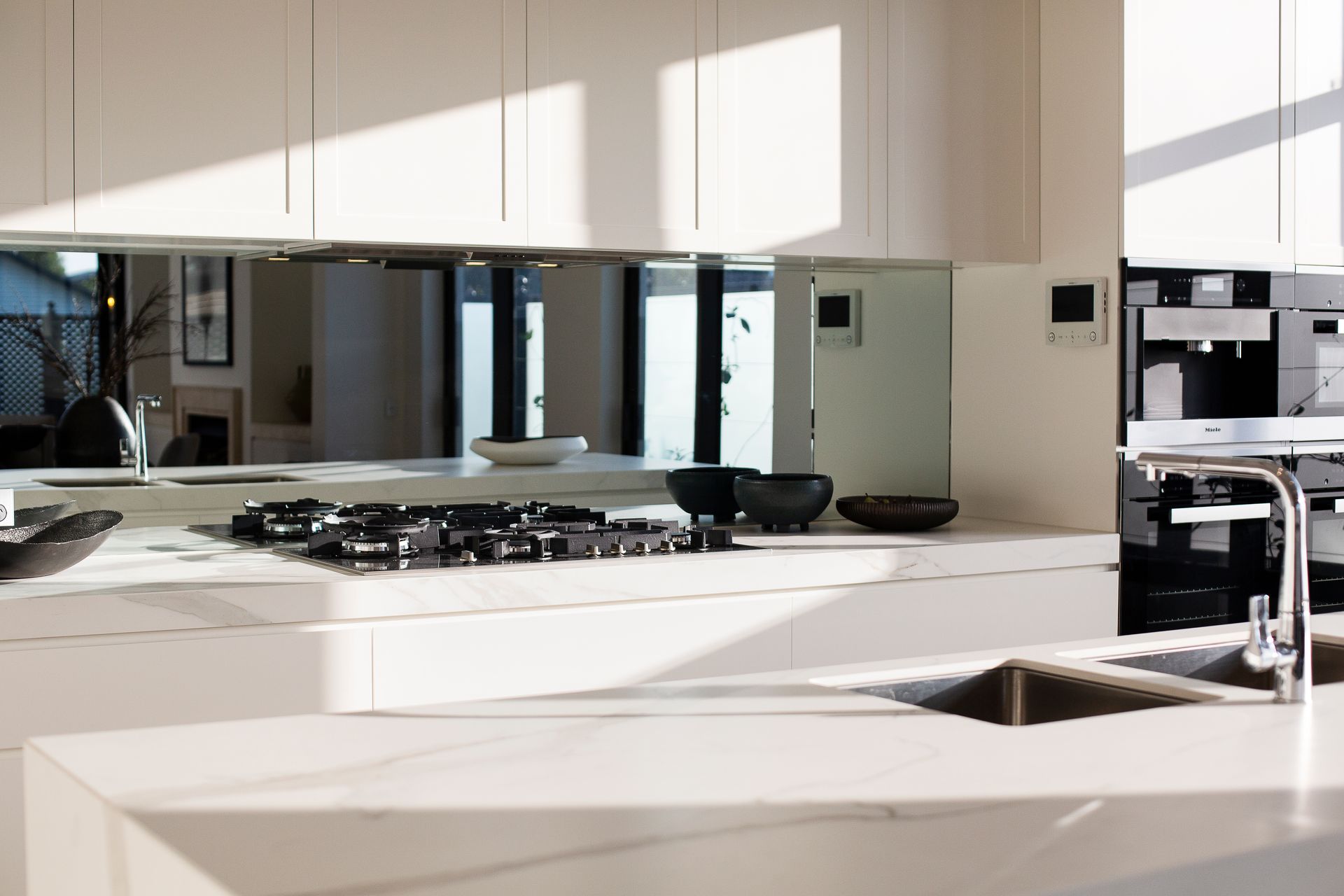 A kitchen mirror splashbackwith a stove top oven and a sink