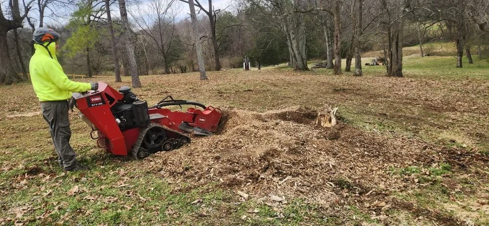 A man is using a stump grinder to remove a tree stump in a field.