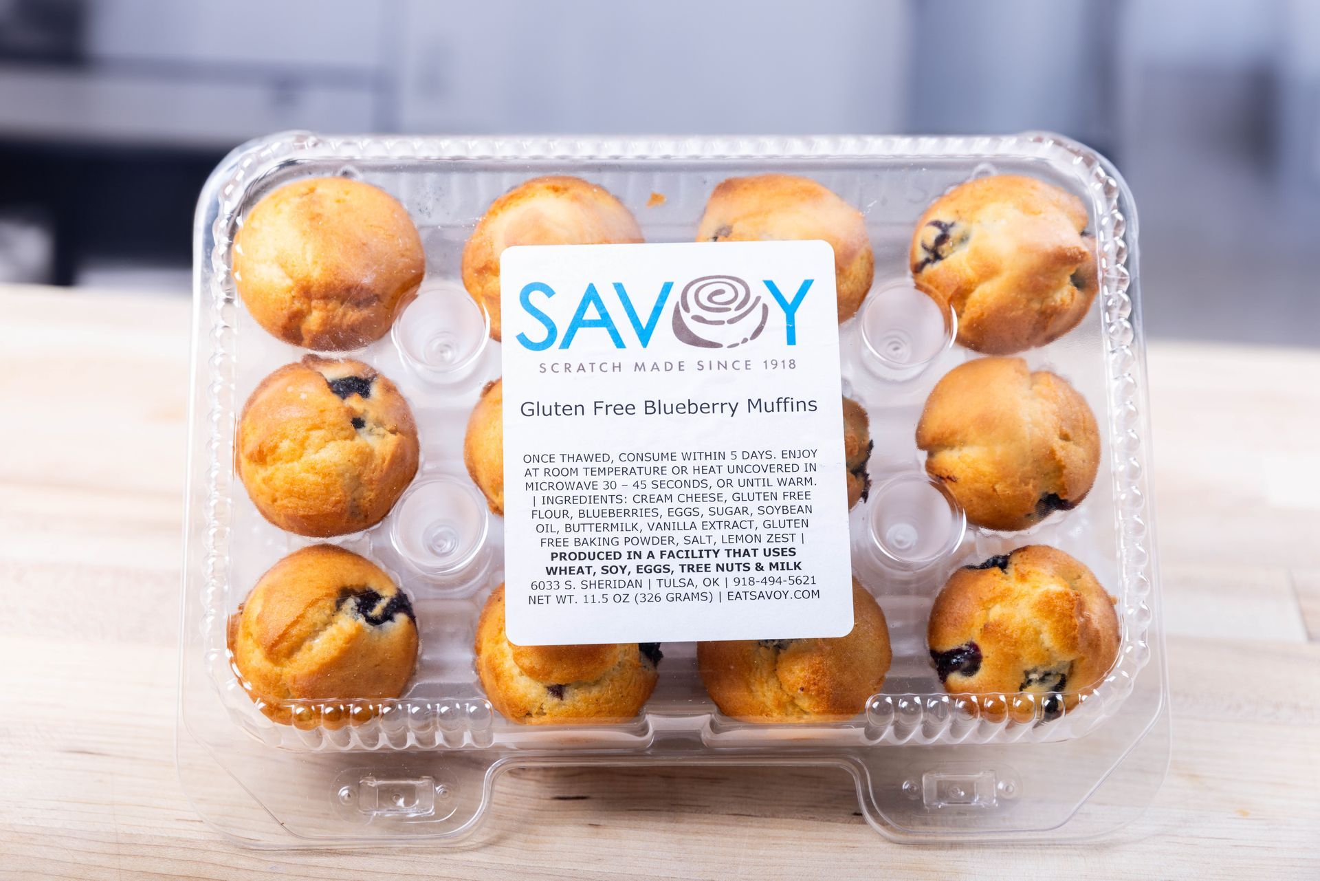 A plastic container of savoy gluten-free blueberry muffins on a wooden table.