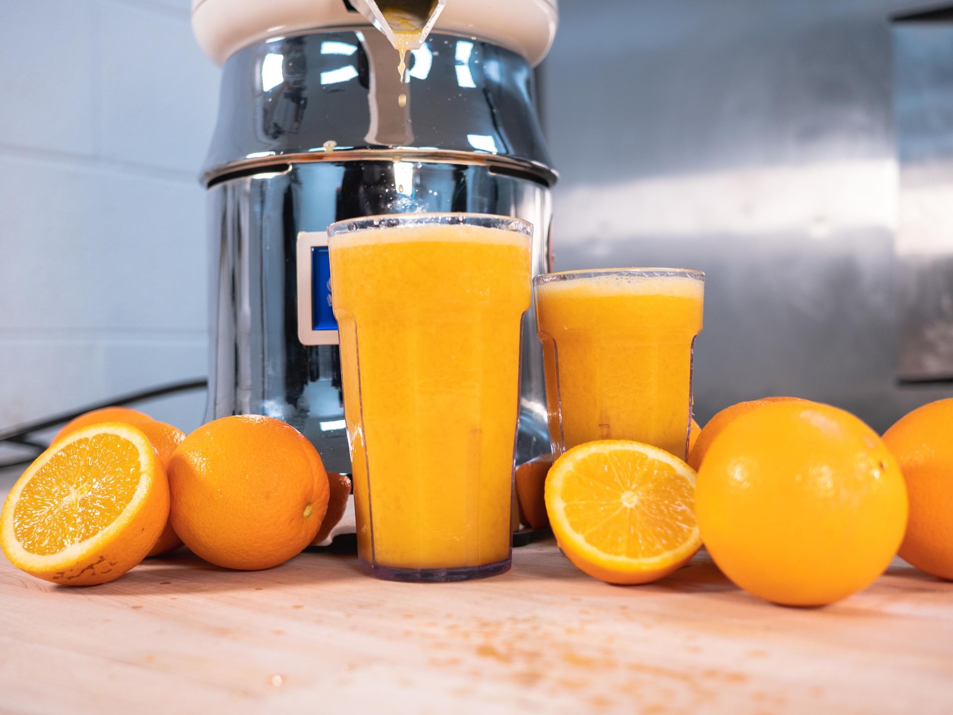 A glass of orange juice is being poured into a glass next to oranges.