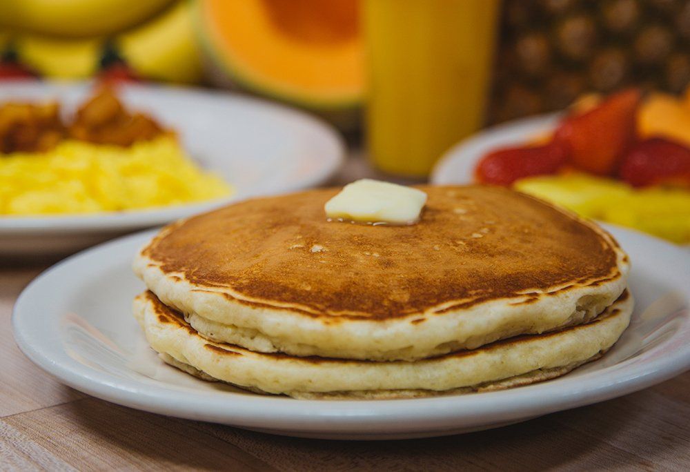 A stack of pancakes with butter on top on a white plate.