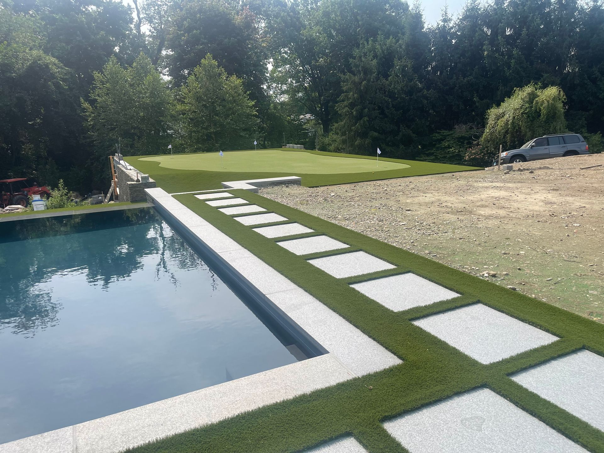 Modern backyard with rectangular pool, stone stepping path, and lawn beside a gravel area and trees