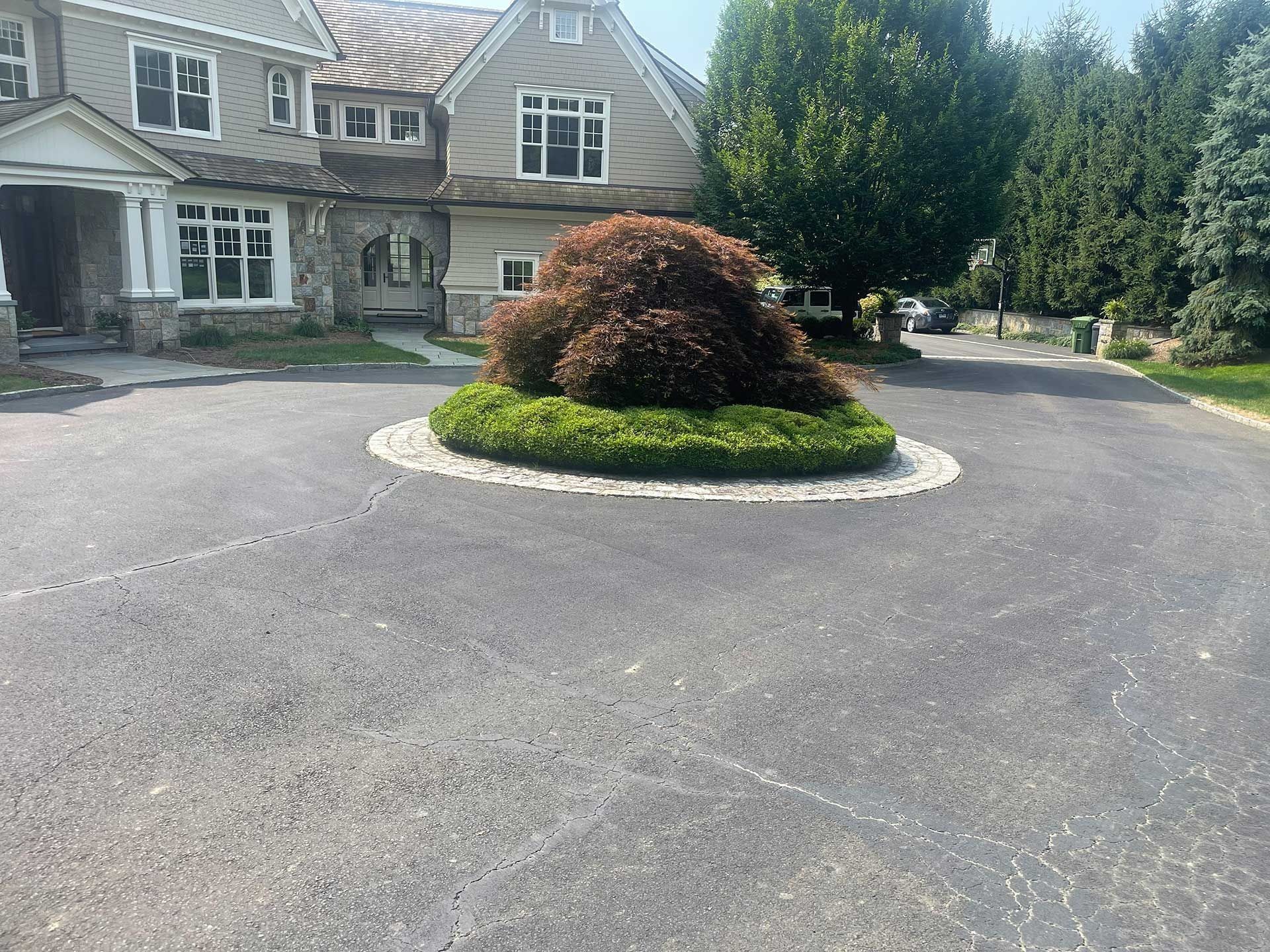 Stone house entrance with circular driveway and landscaped island of shrubs and flowers