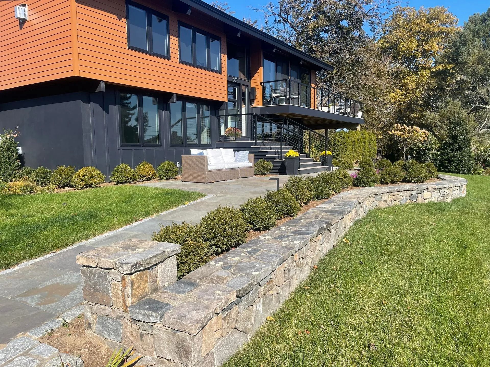 Modern house with orange and dark siding, stone walkway, and landscaped lawn in front