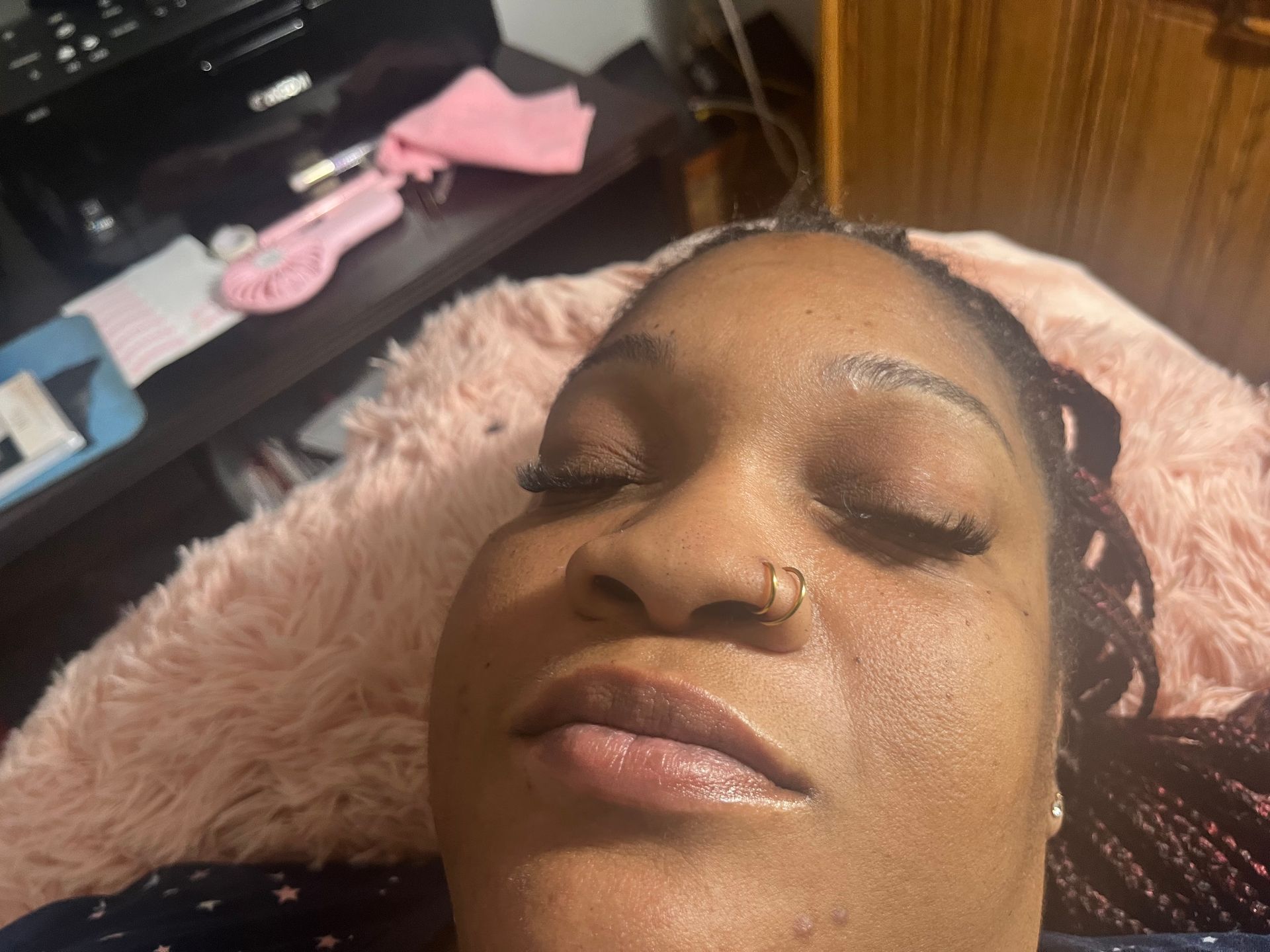 Woman with closed eyes, lying on a pink blanket, possibly getting a beauty treatment.