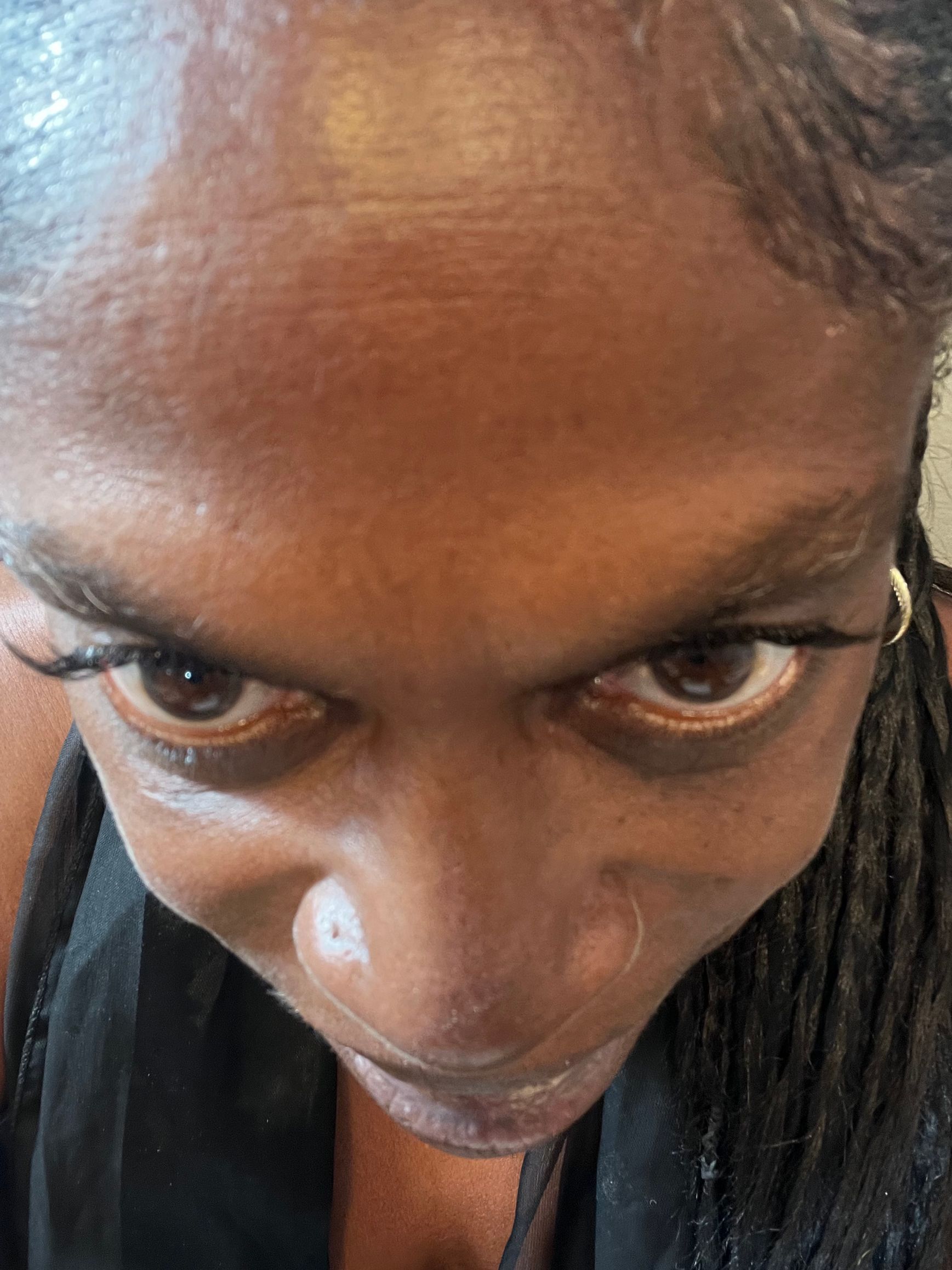 A person looking down at the camera, dark skin, braided hair, and focused eyes.