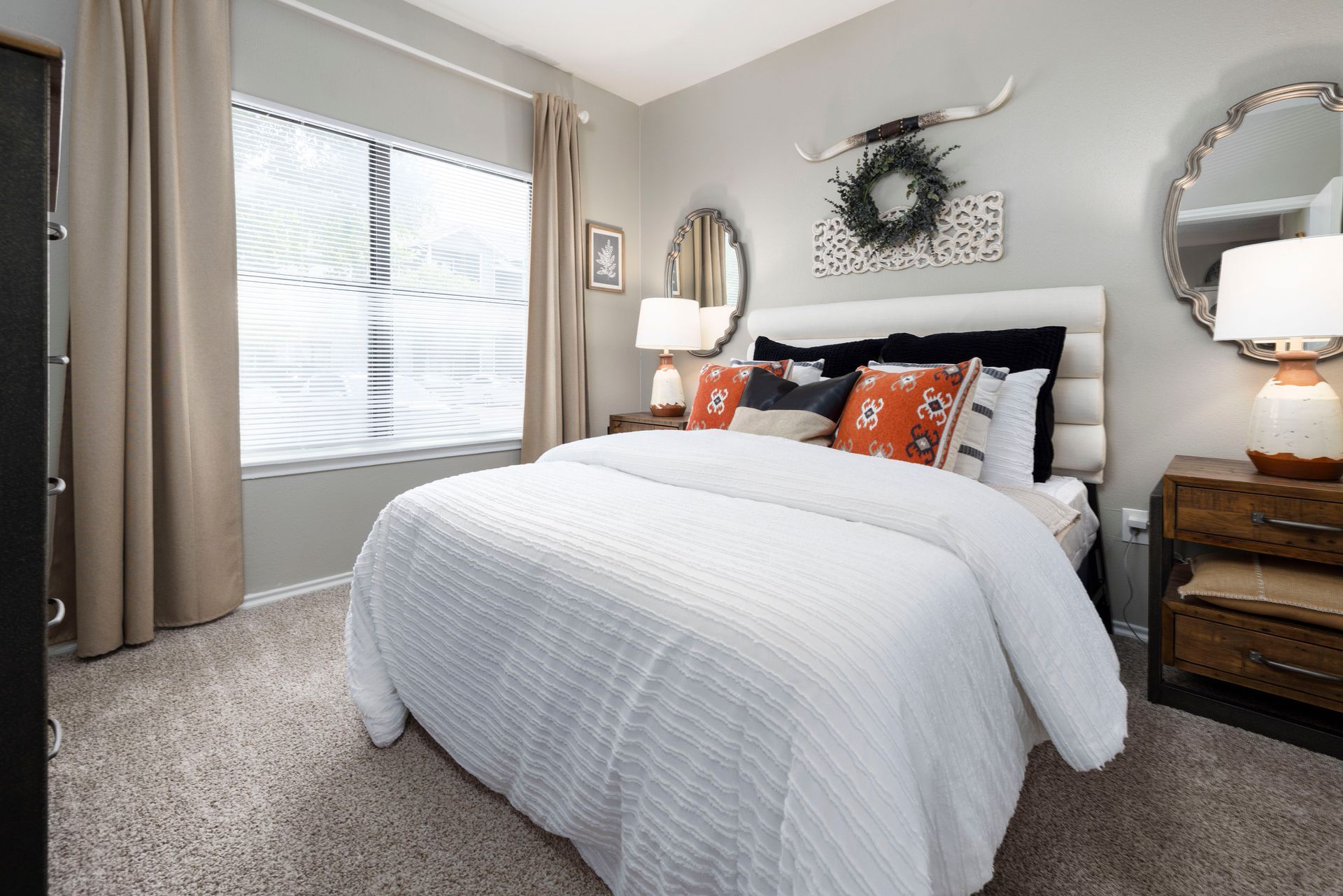 A bedroom with a bed , dresser , mirror and window.