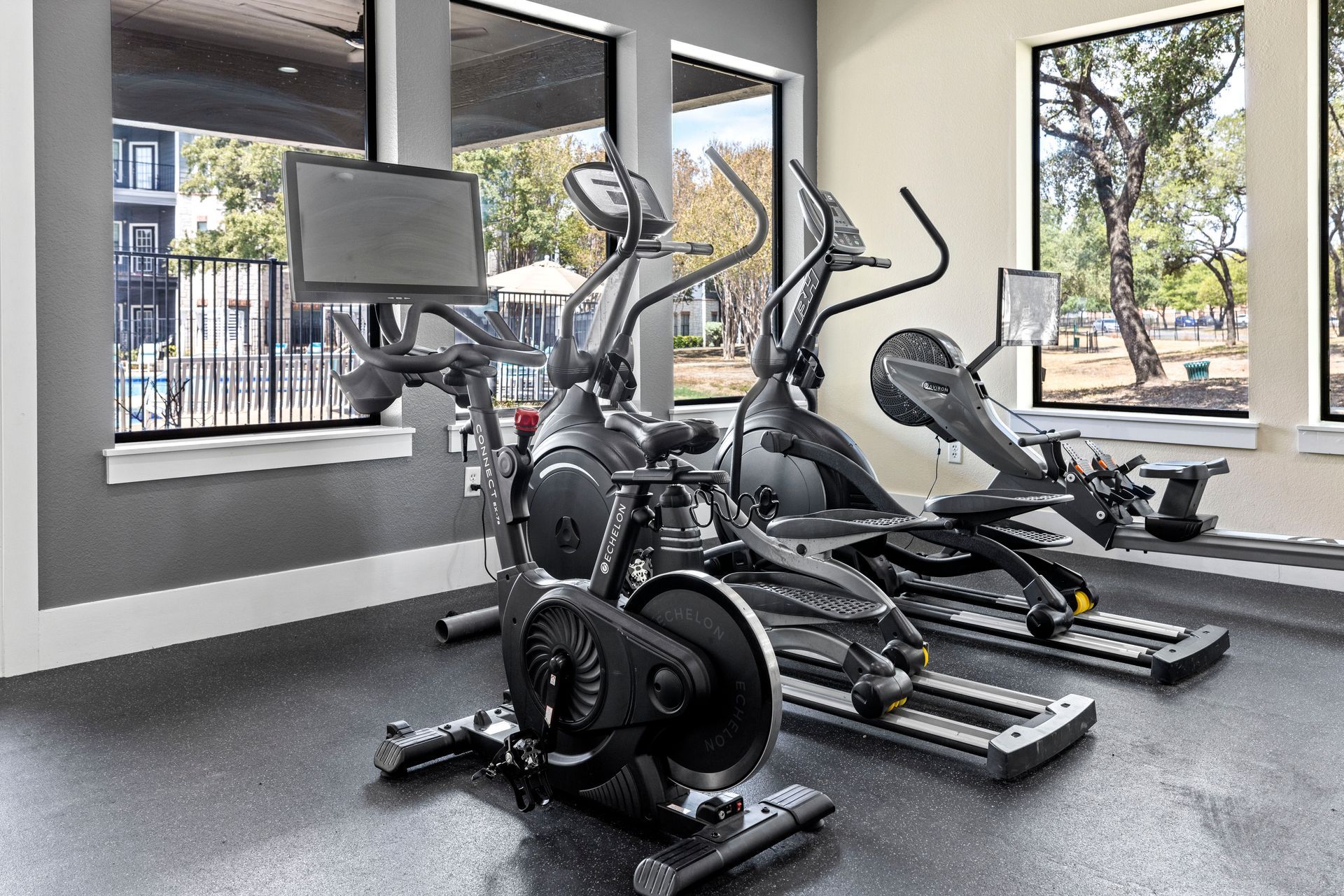 A gym with a lot of exercise equipment and a lot of windows.