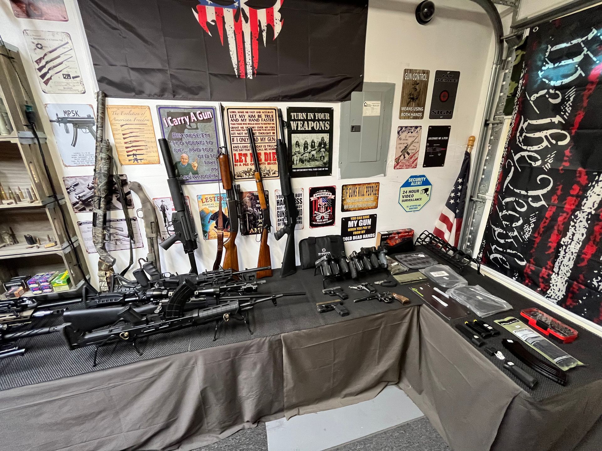 A table displaying various firearms with flags and signs in a garage setting.