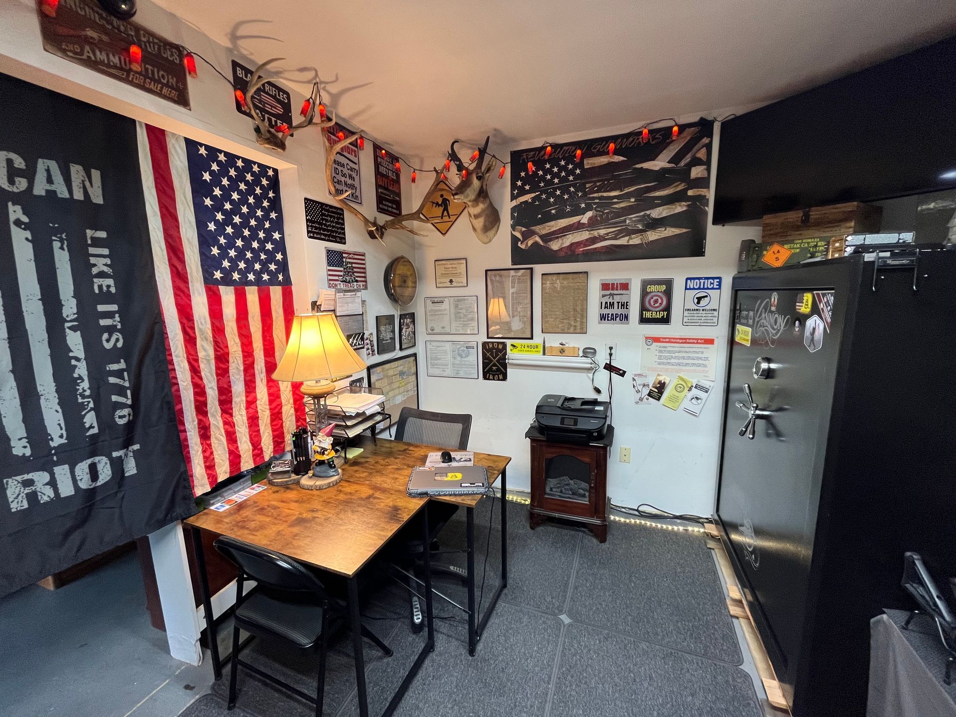 A cluttered office with an American flag and a desk. Flags, documents, and a safe adorn the walls.