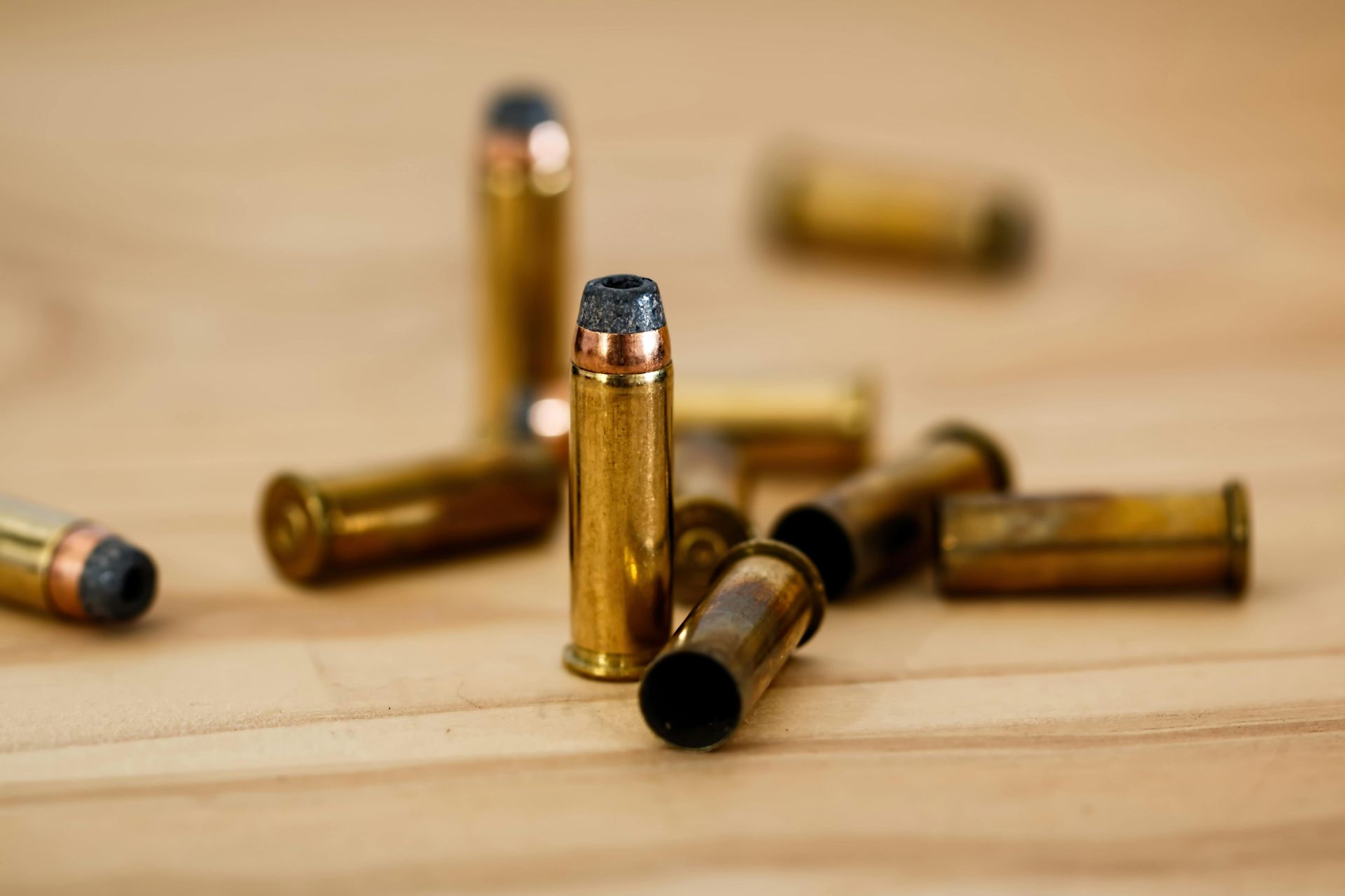 Scattered brass bullet casings with copper-colored tips on a light wooden surface.