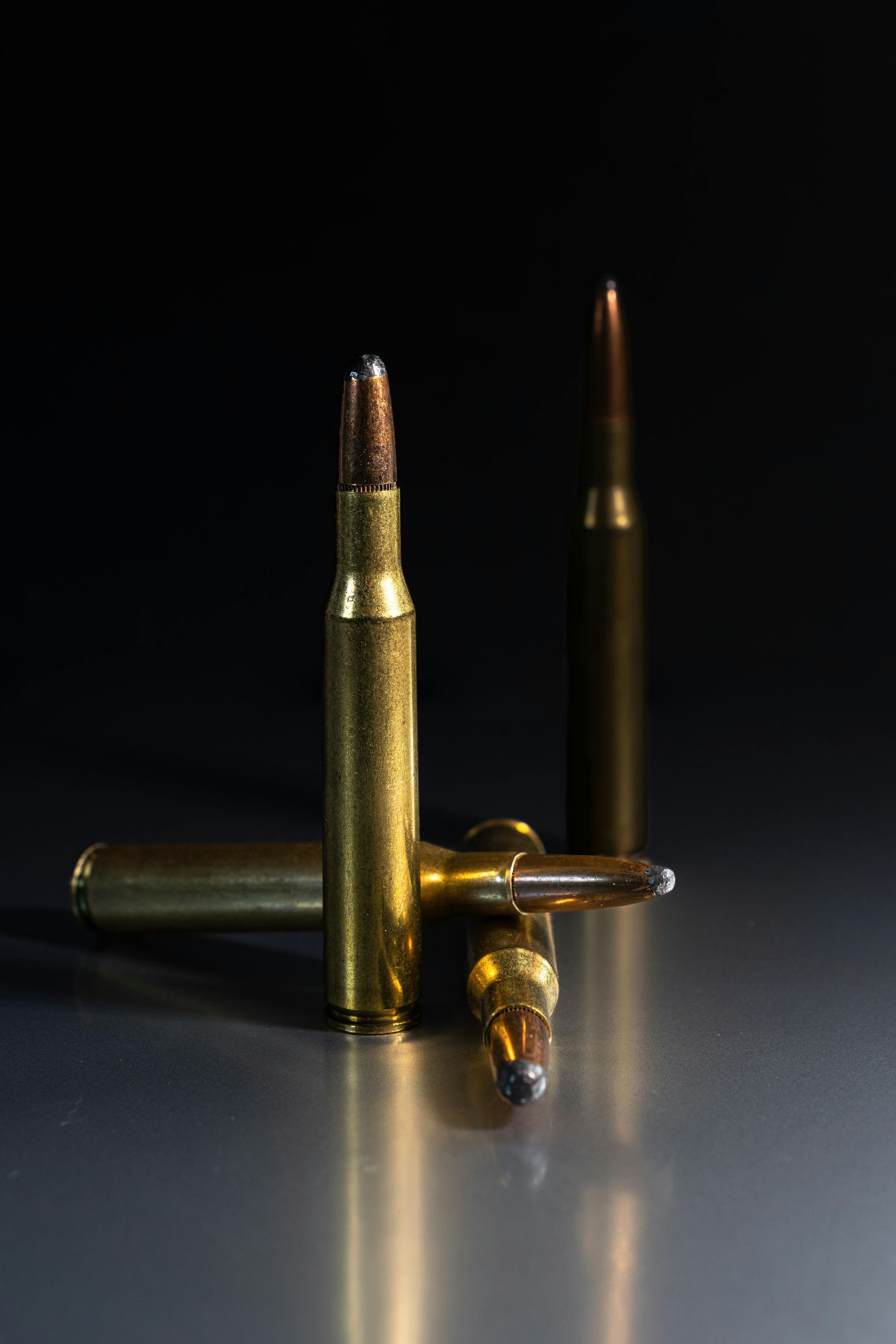 Three rifle bullets on a reflective surface, brass casings and pointed tips, against a dark background.