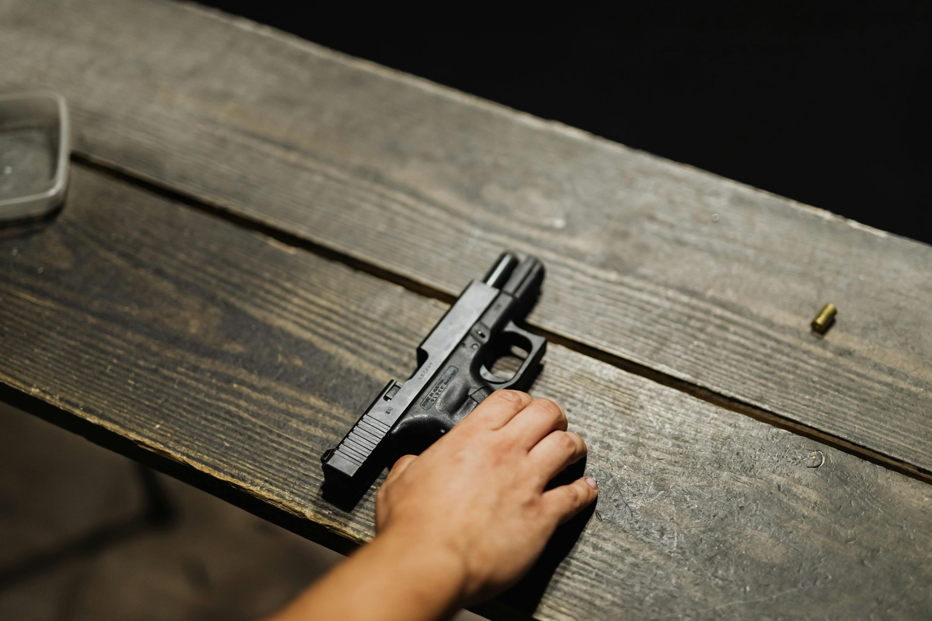 A handgun on a wooden surface next to a hand and a bullet.