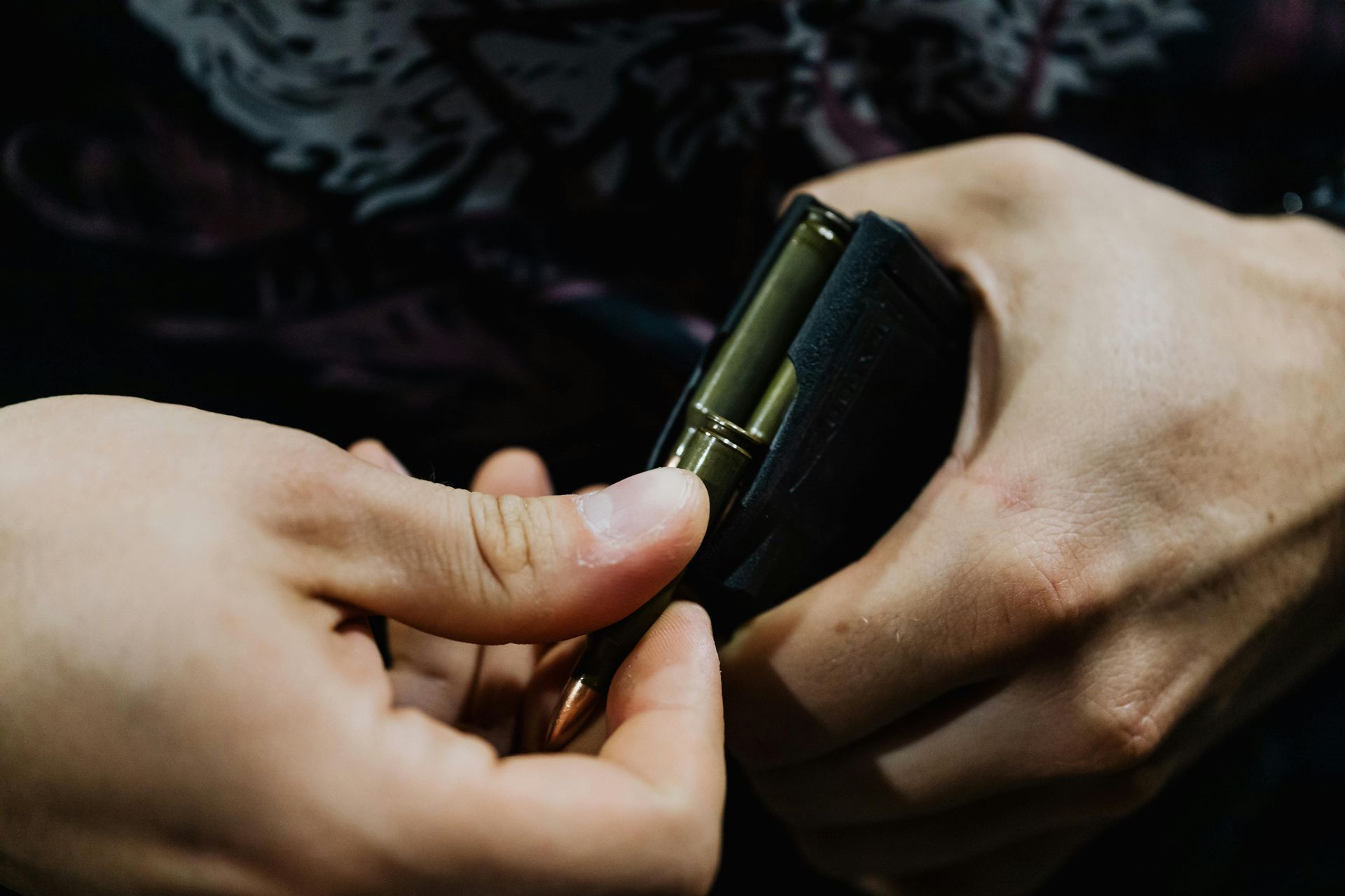 Person loads bullets into a magazine, close-up on hands and ammunition.