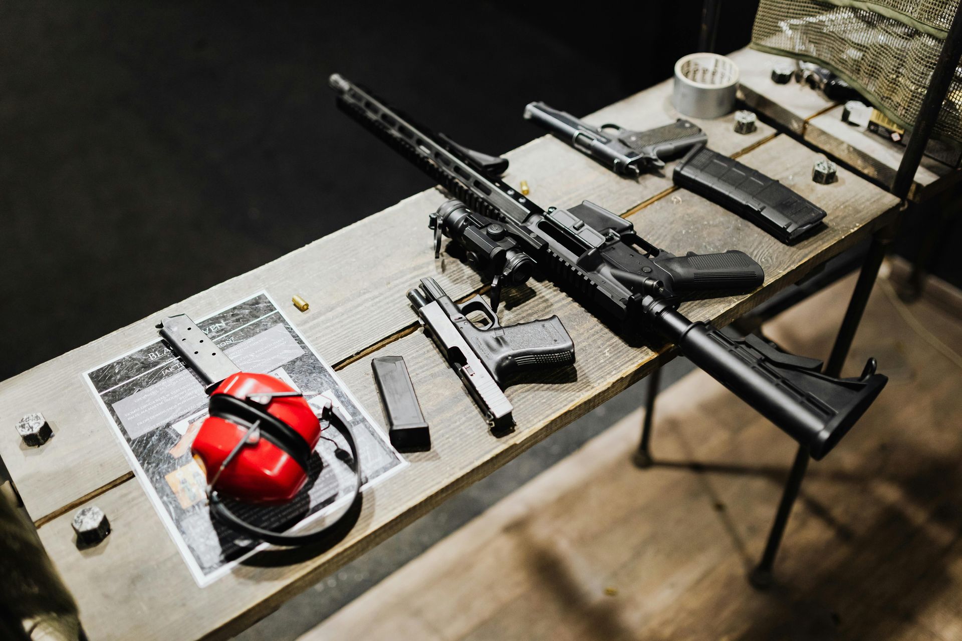 A table with various firearms and accessories, including a rifle, pistols, and a headset.