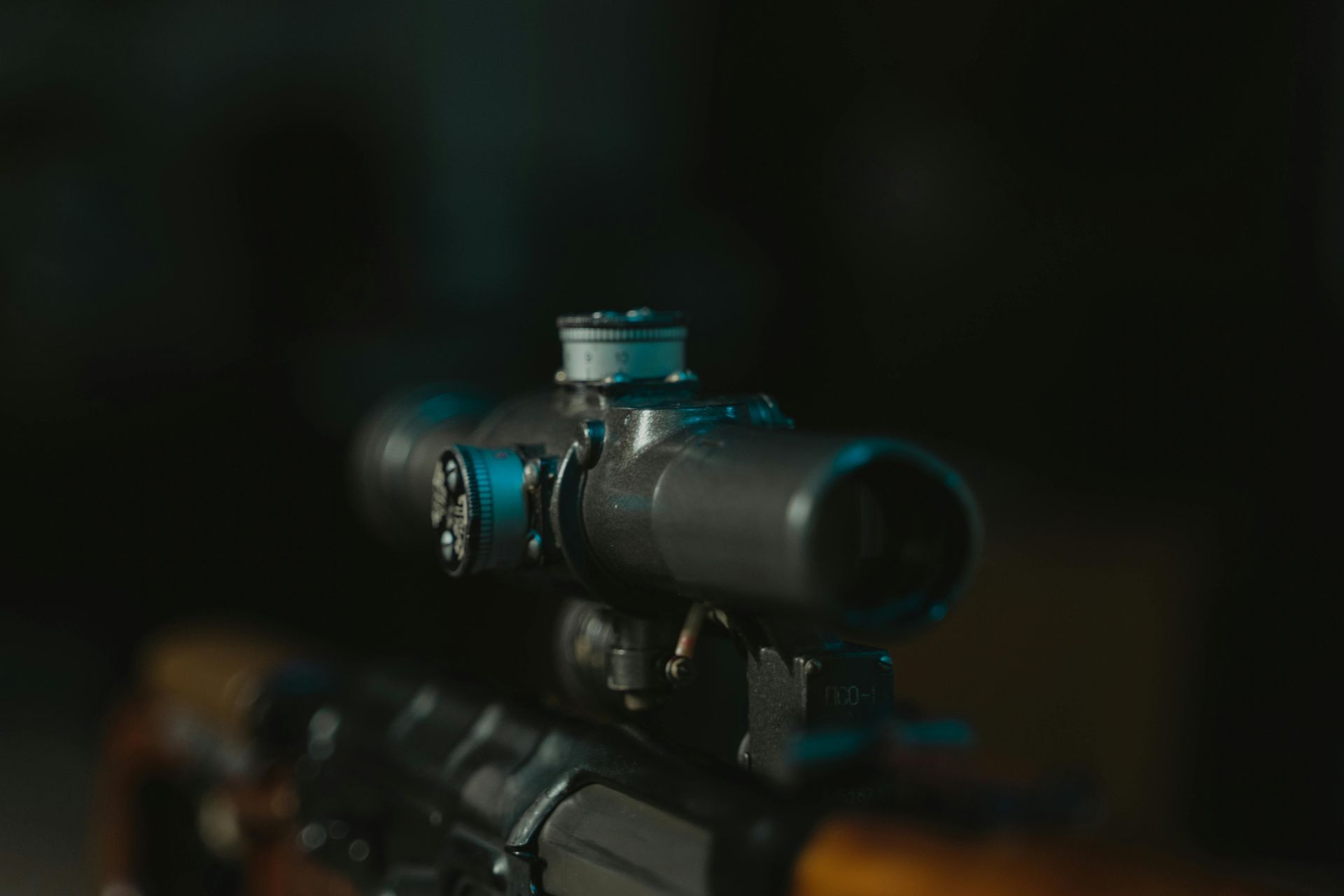 Sniper rifle scope, close-up. Black optic on wooden stock, dark background, aiming view.