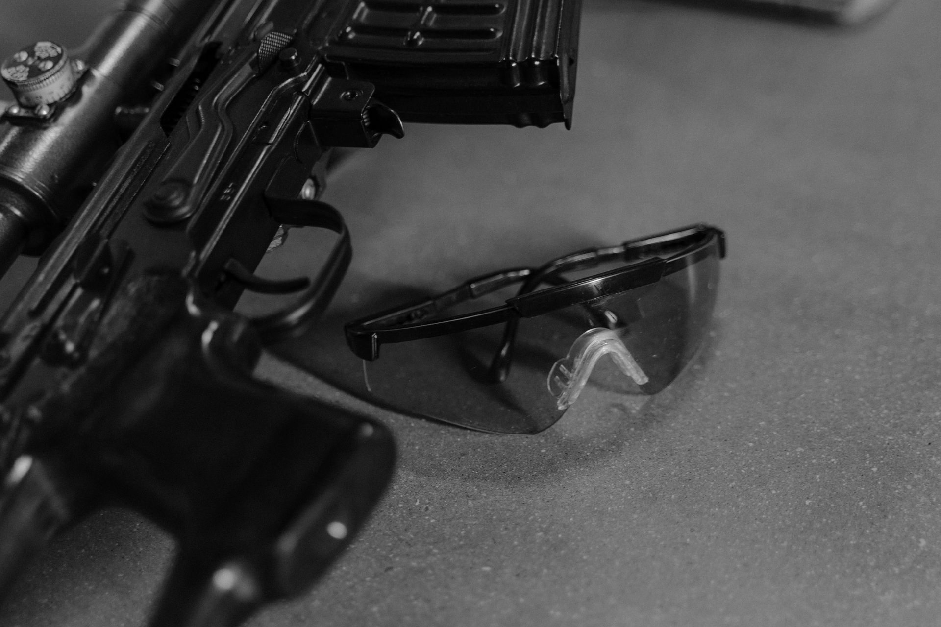 A black and white close-up of a gun and safety glasses.