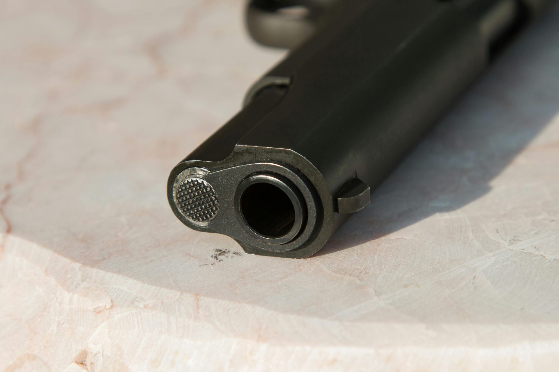 Close-up of a black handgun's barrel resting on a light-colored surface.