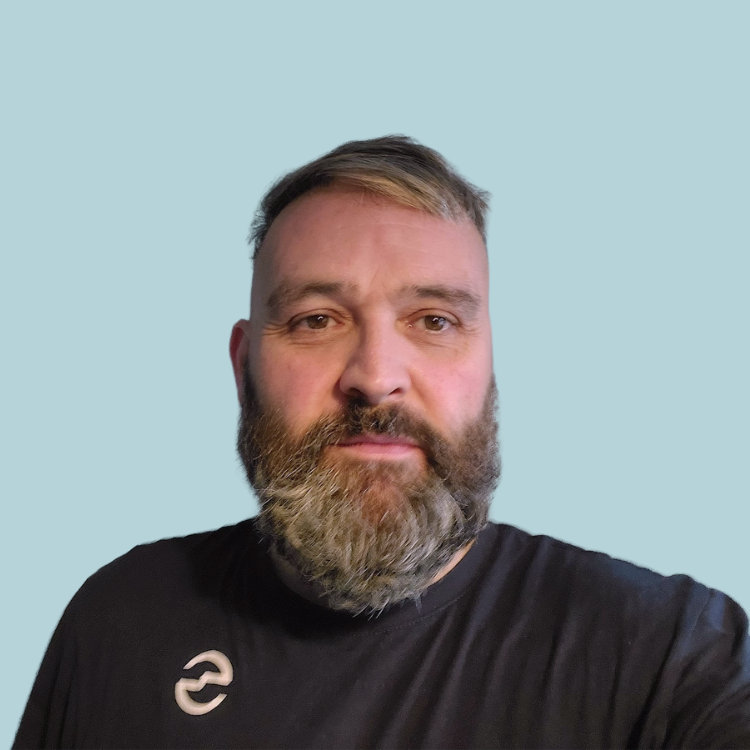 Man with a full salt and pepper beard wearing a black shirt against a light blue background.
