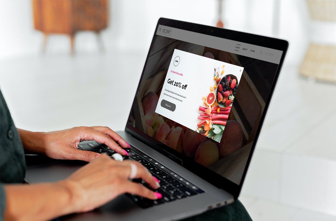 Person using a laptop, with a popup advertisement for a fruit-based product displayed on screen, in a light-filled interior.