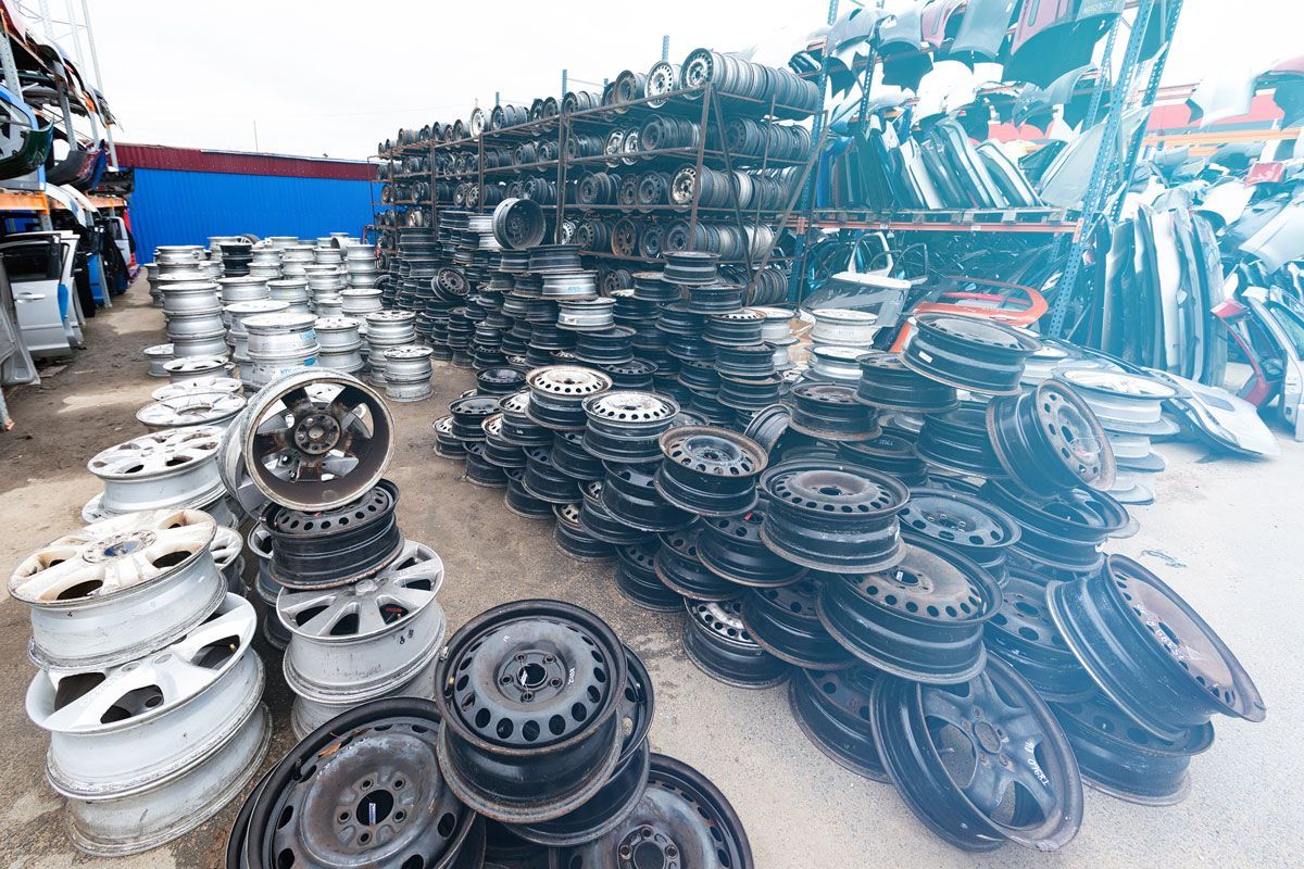 Stacks of used car wheels at a junkyard, some painted silver, some black, outdoors.