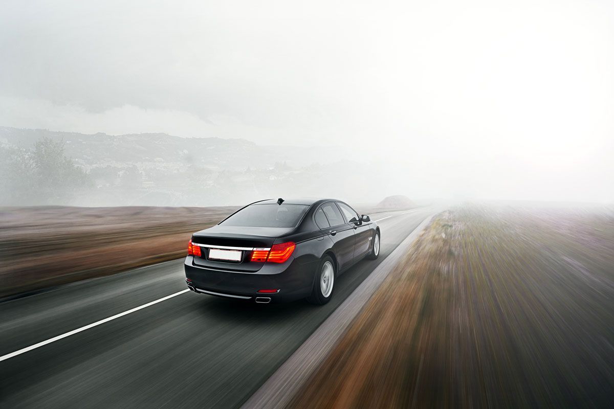 Black car driving on a wet road through a foggy landscape.