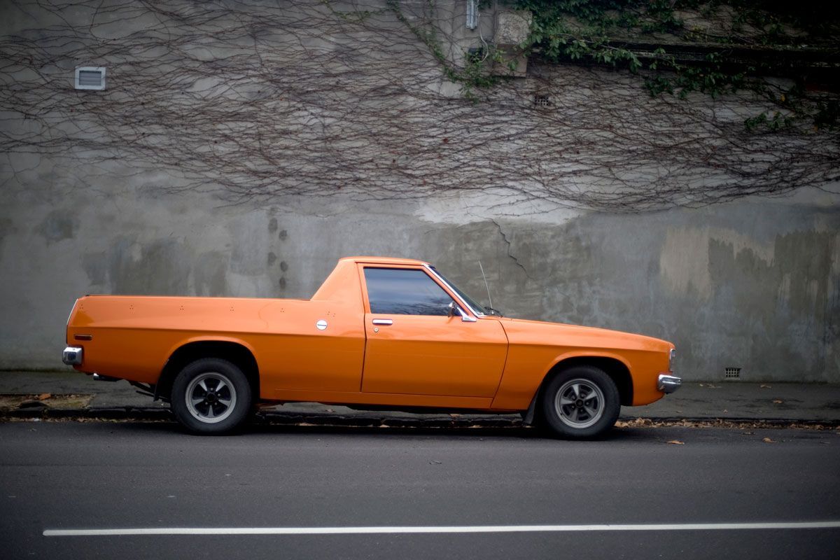 Orange utility vehicle parked on a road, in front of a wall covered in ivy.