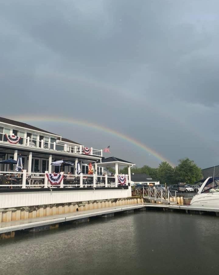 A boat is docked in front of a building with a rainbow in the sky.