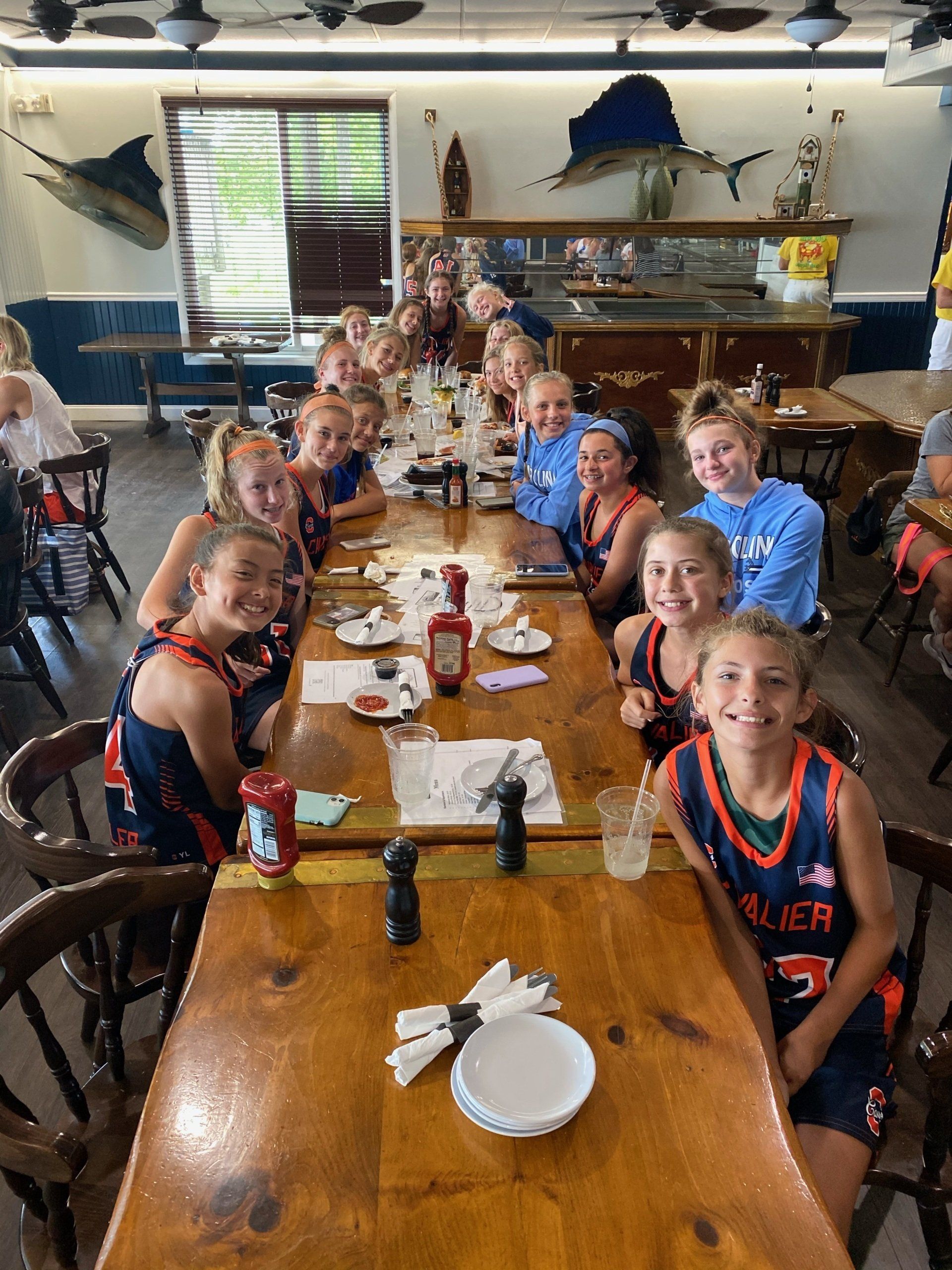 A group of young girls are sitting at a long wooden table in a restaurant.