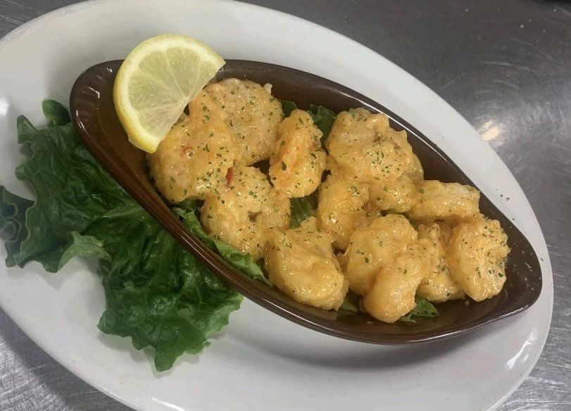 A plate of shrimp with a slice of lemon on top.