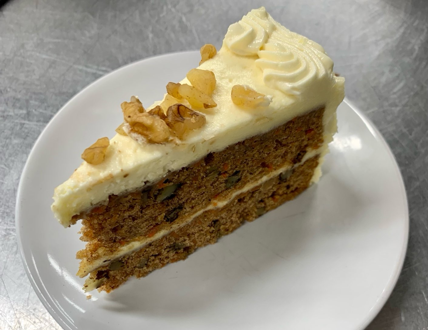 A slice of carrot cake with whipped cream and walnuts on a white plate.