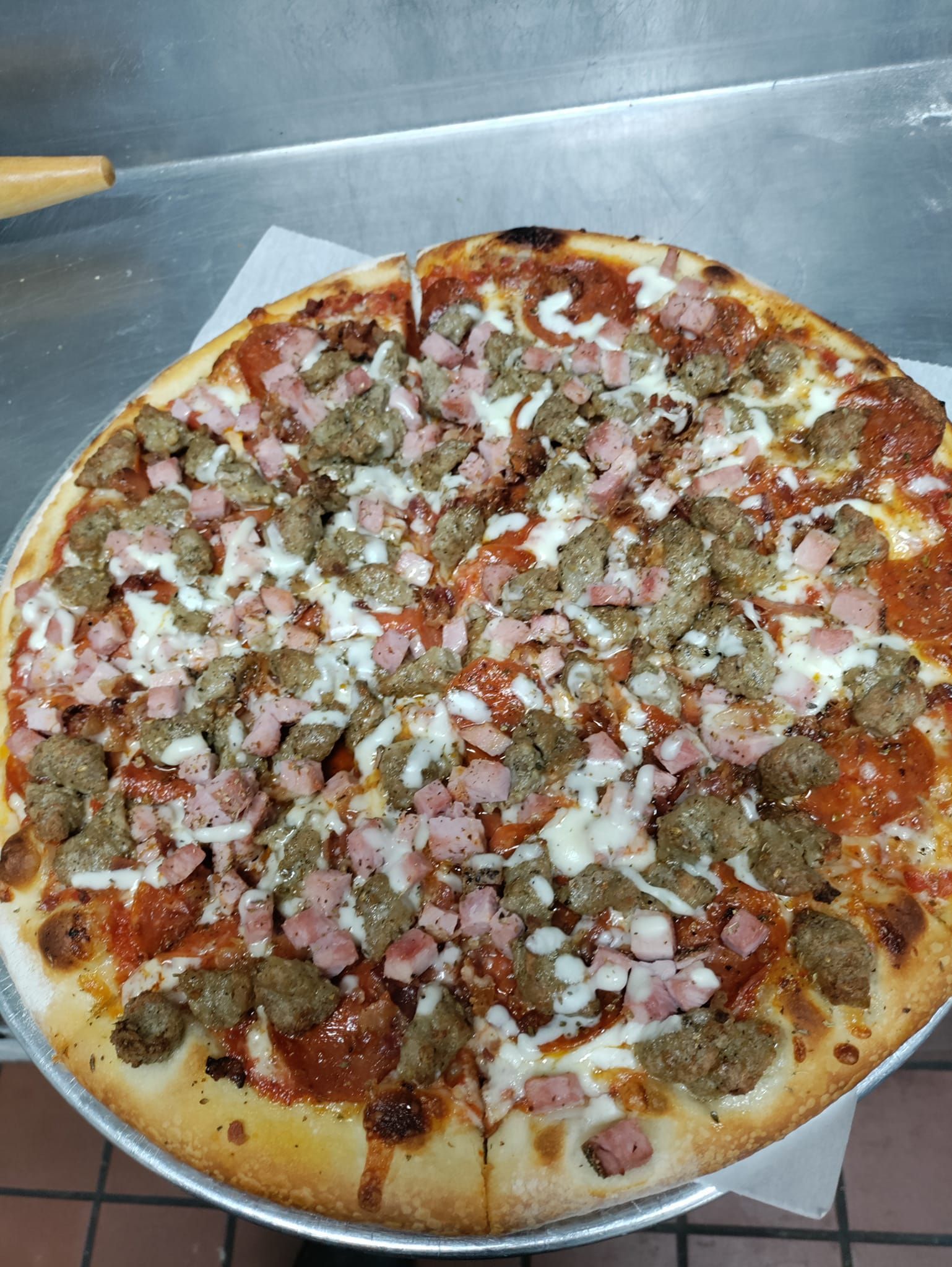 A pizza with pepperoni , ham , sausage and cheese on a pan.