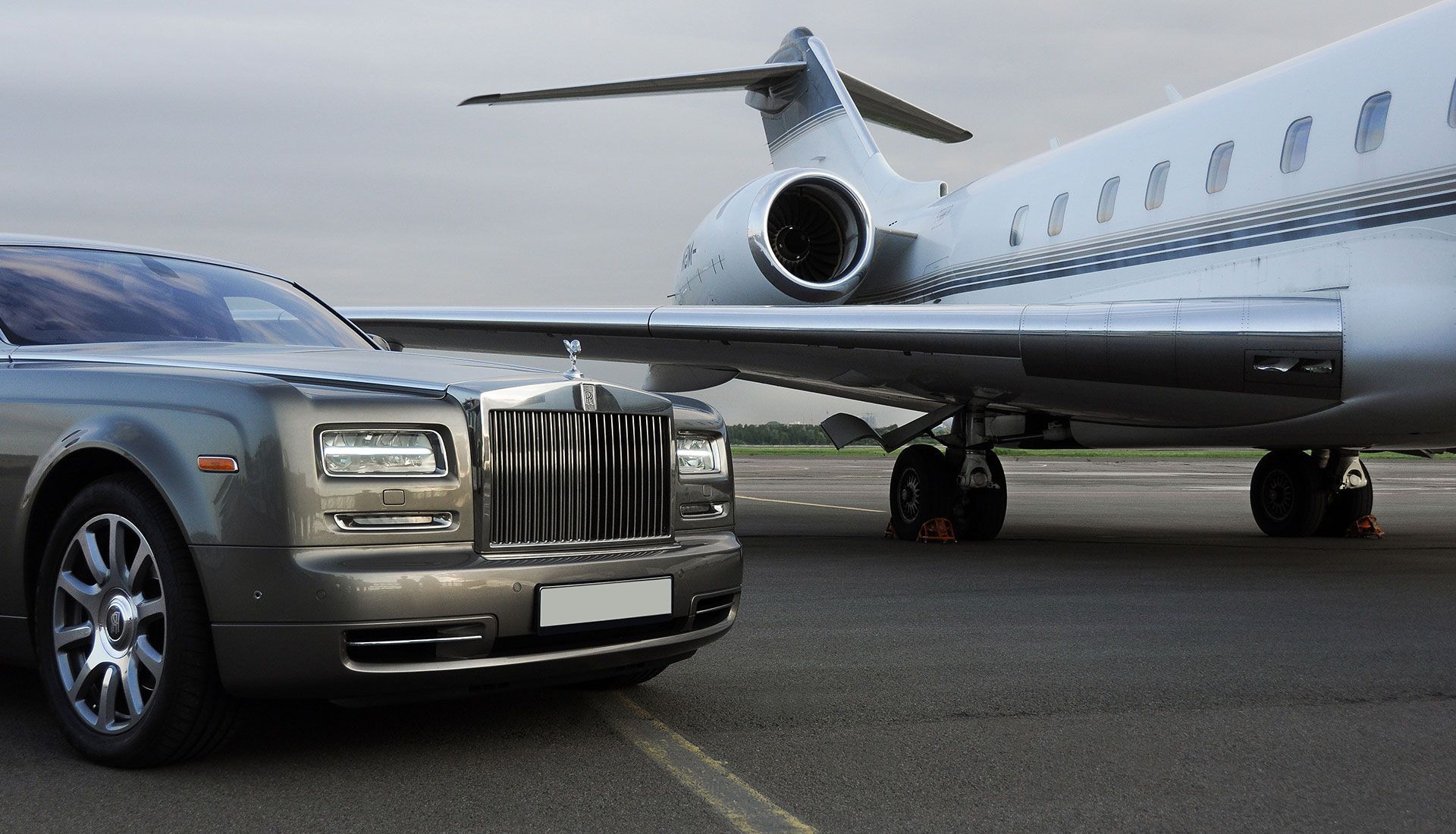 Gray Rolls Royce parked next to a private jet on a tarmac.