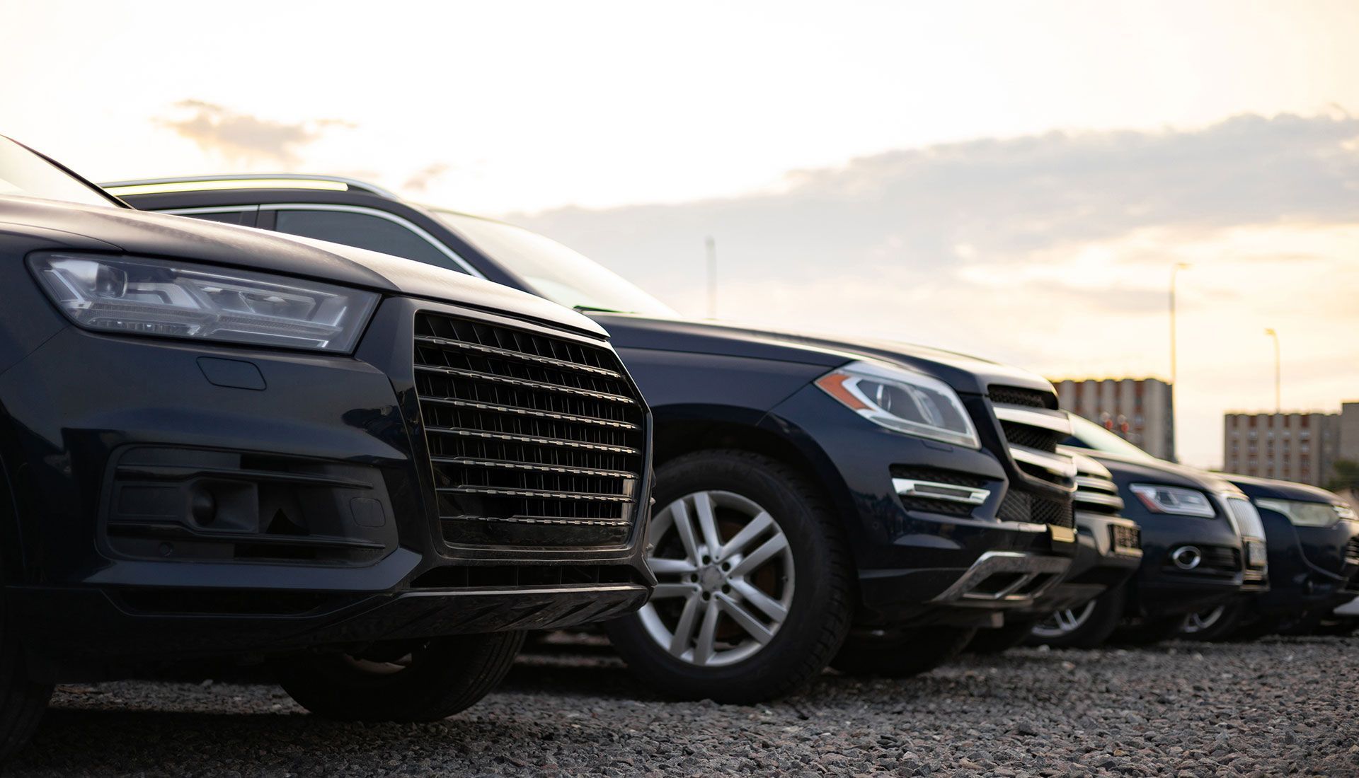 Cars parked in a row, dark colors, in an outdoor lot.