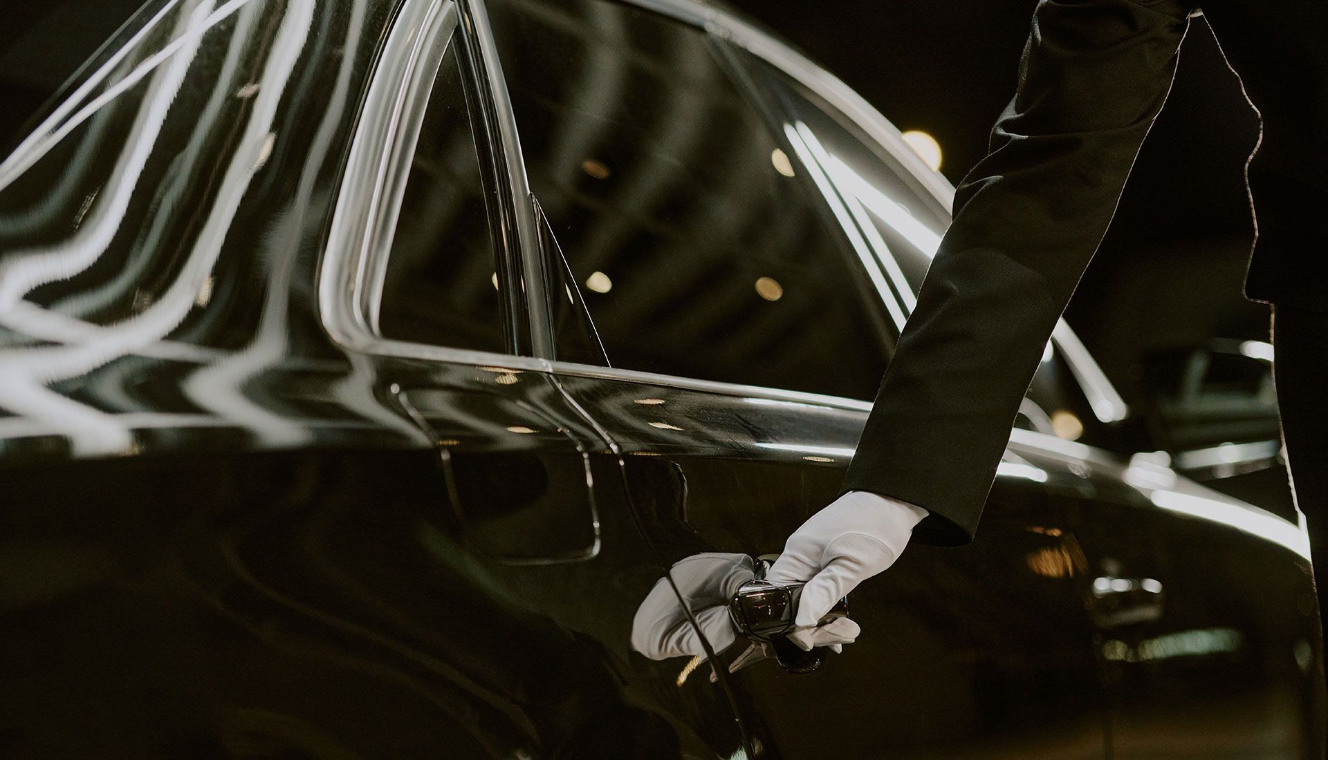 A gloved hand opening a black car door at night.