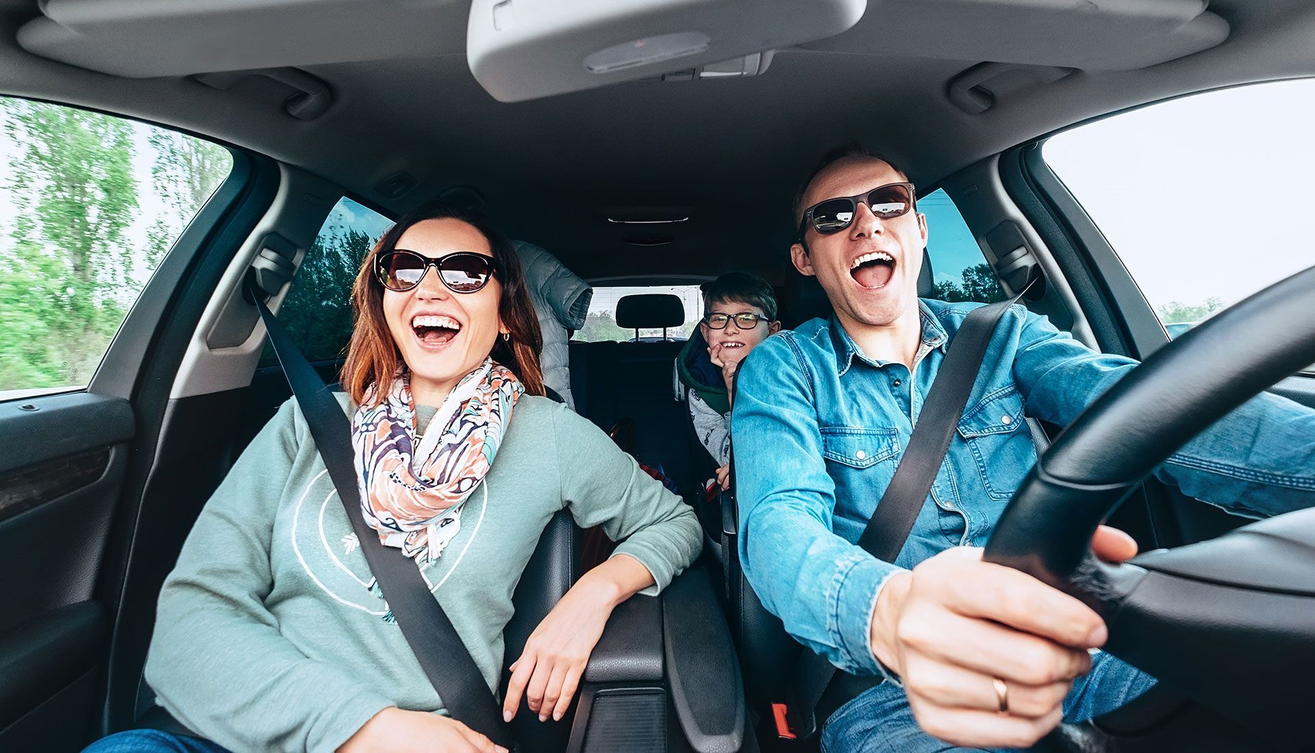 Family in car laughing and wearing sunglasses; front seats in focus.