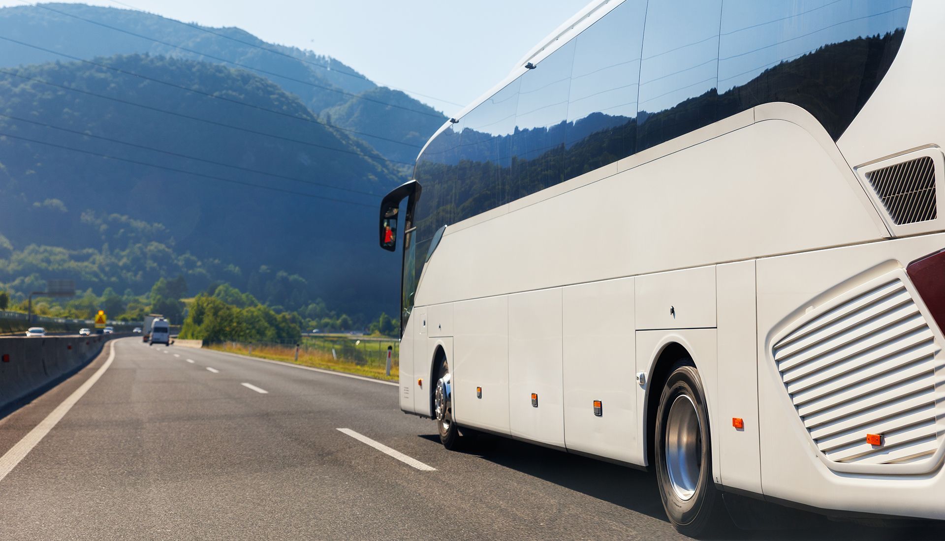 White tour bus on highway with mountains in background.