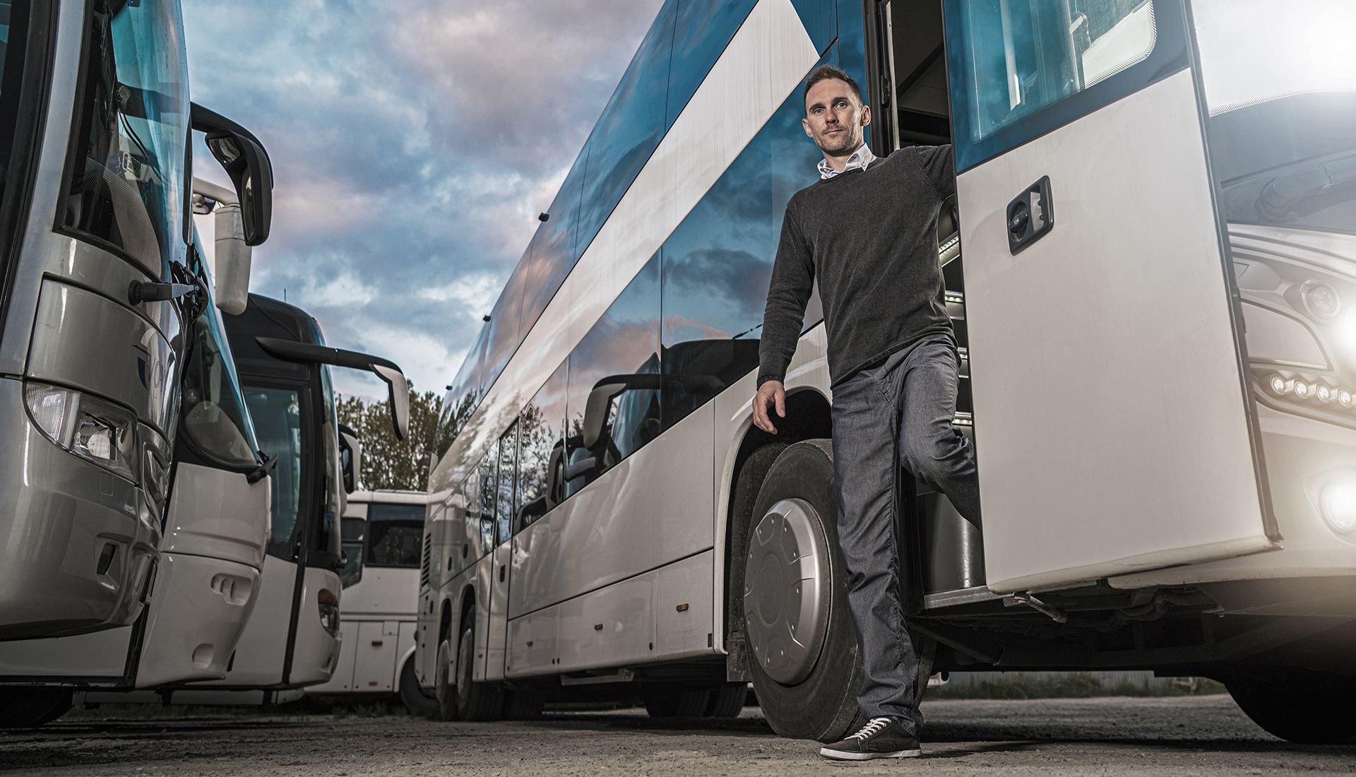 Man exiting a bus parked among other buses under a cloudy sky.