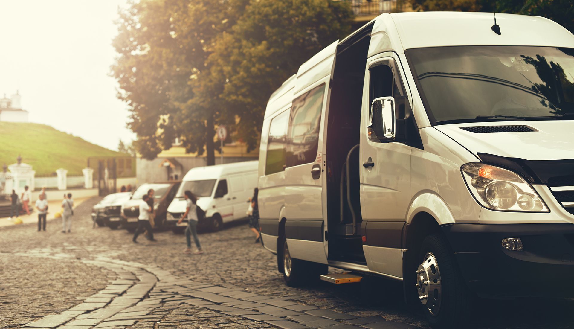 White passenger van with open door parked on cobblestone street.