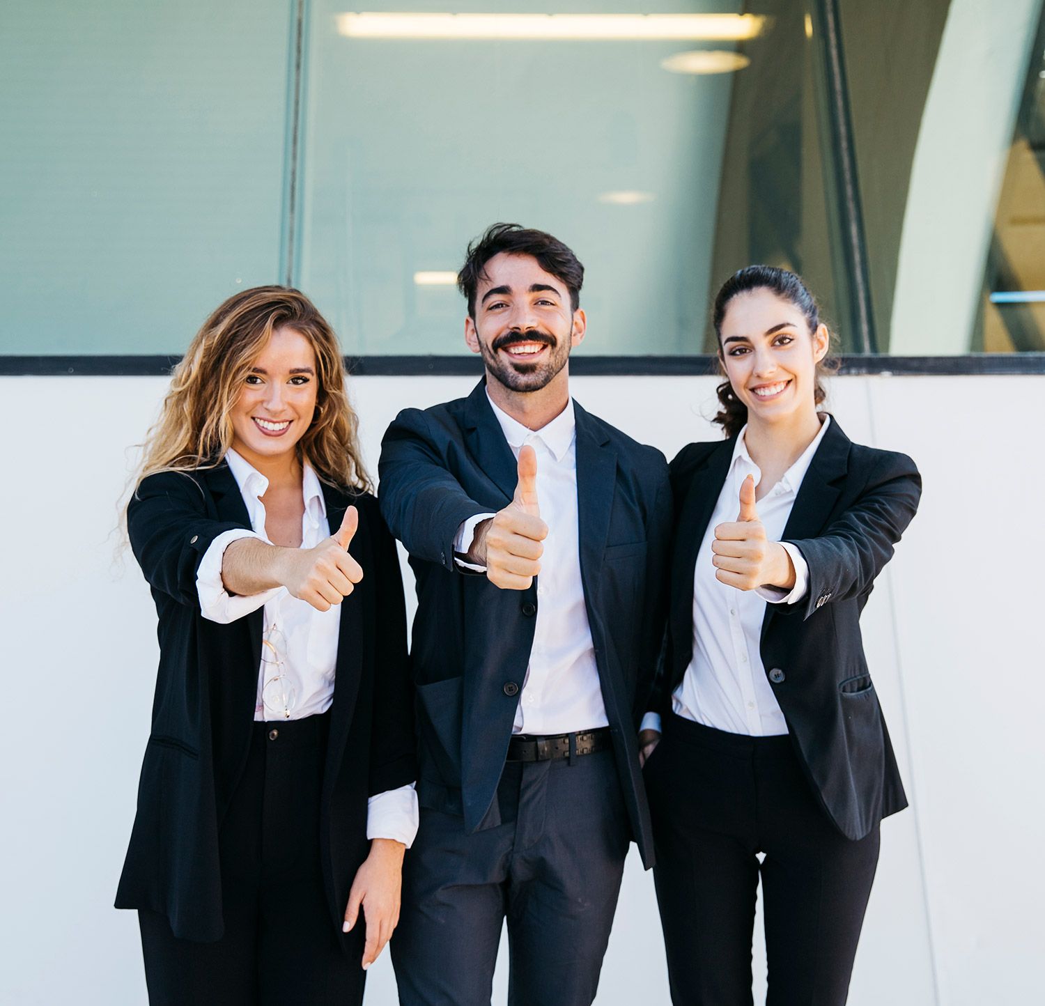 A man and two women are giving a thumbs up in front of a building.