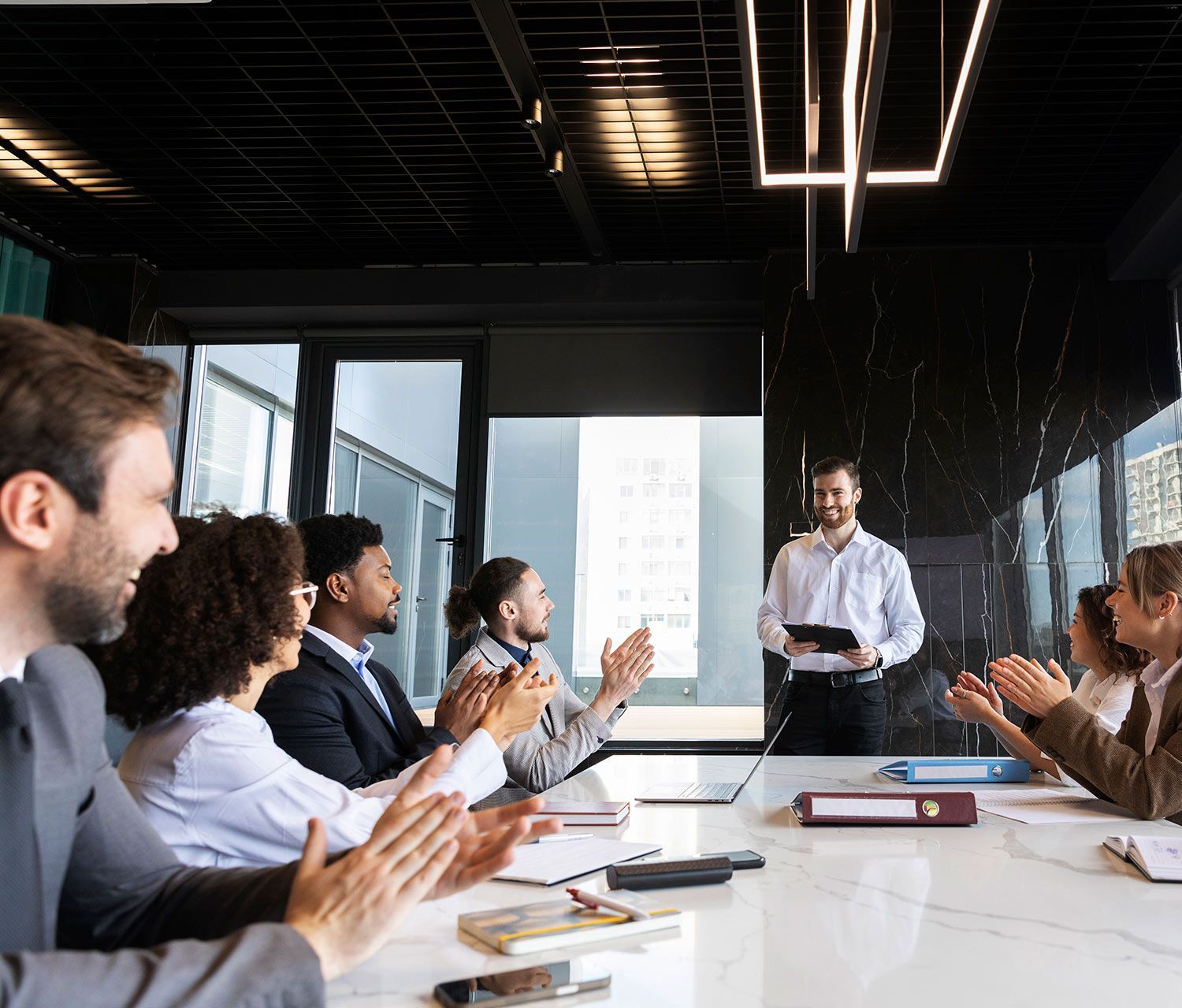 A group of people are sitting around a table in a conference room clapping.