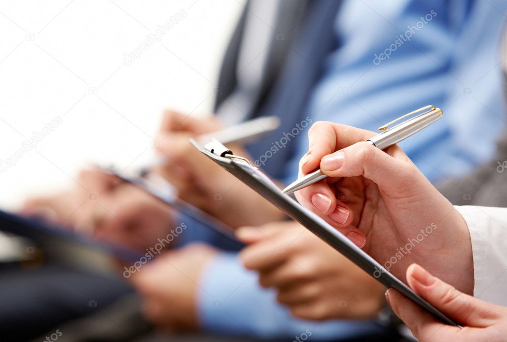 A group of people are sitting in a row holding clipboards and pens.