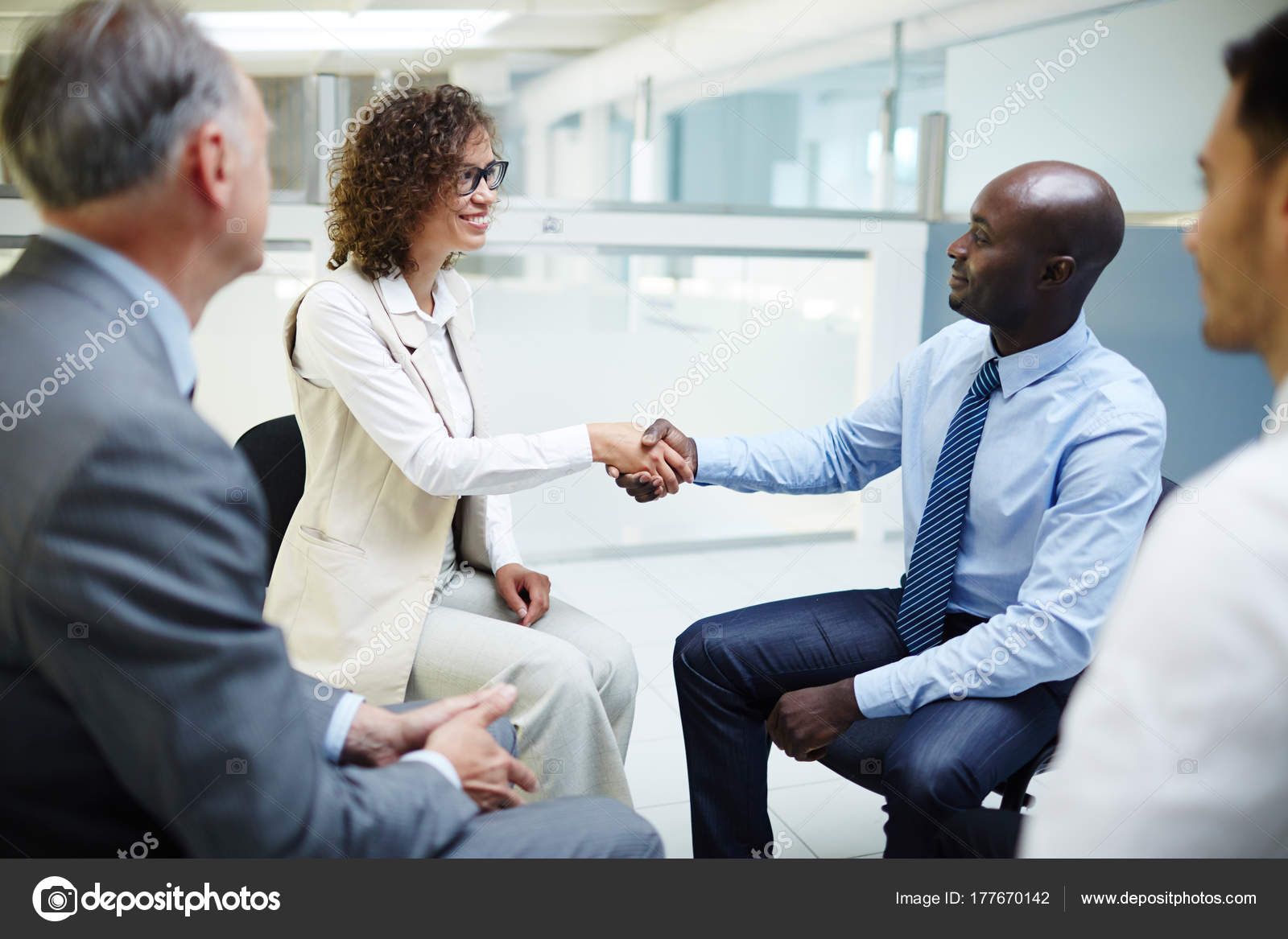 A group of business people are sitting in a circle shaking hands.