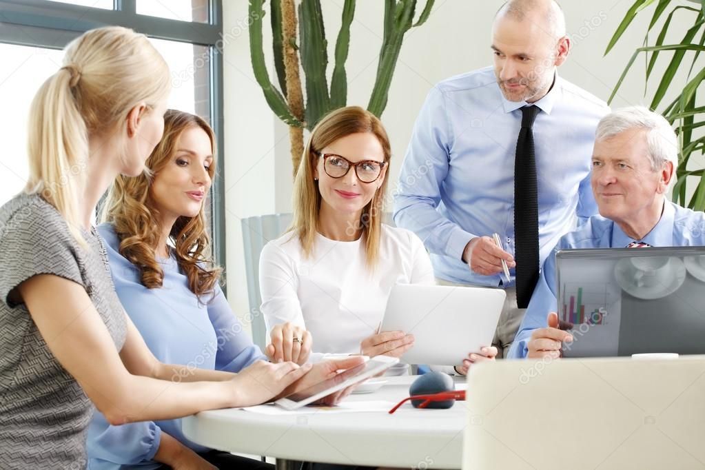 A group of people are sitting around a table looking at a laptop.