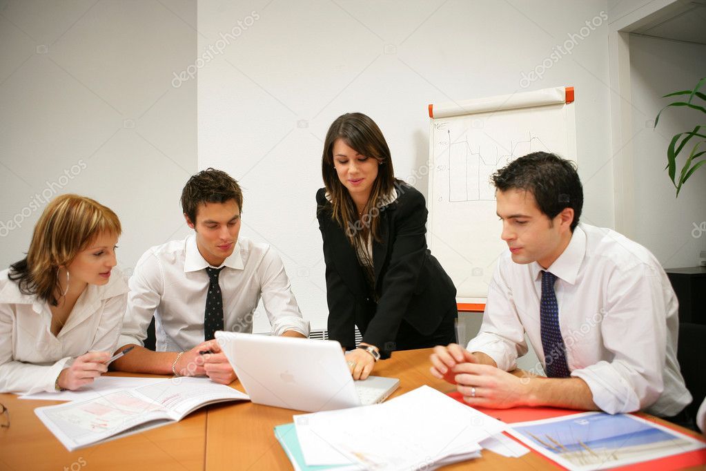 A group of people are sitting around a table looking at a laptop.