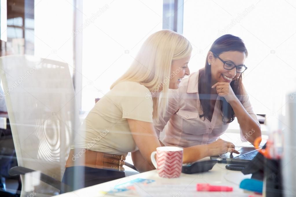 Two women are sitting at a desk looking at a computer screen.