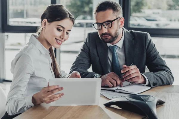 A man and a woman are sitting at a table looking at a tablet.