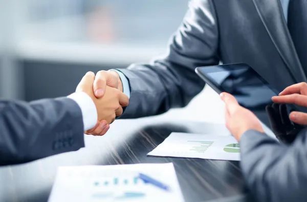 Two business people are shaking hands over a table.