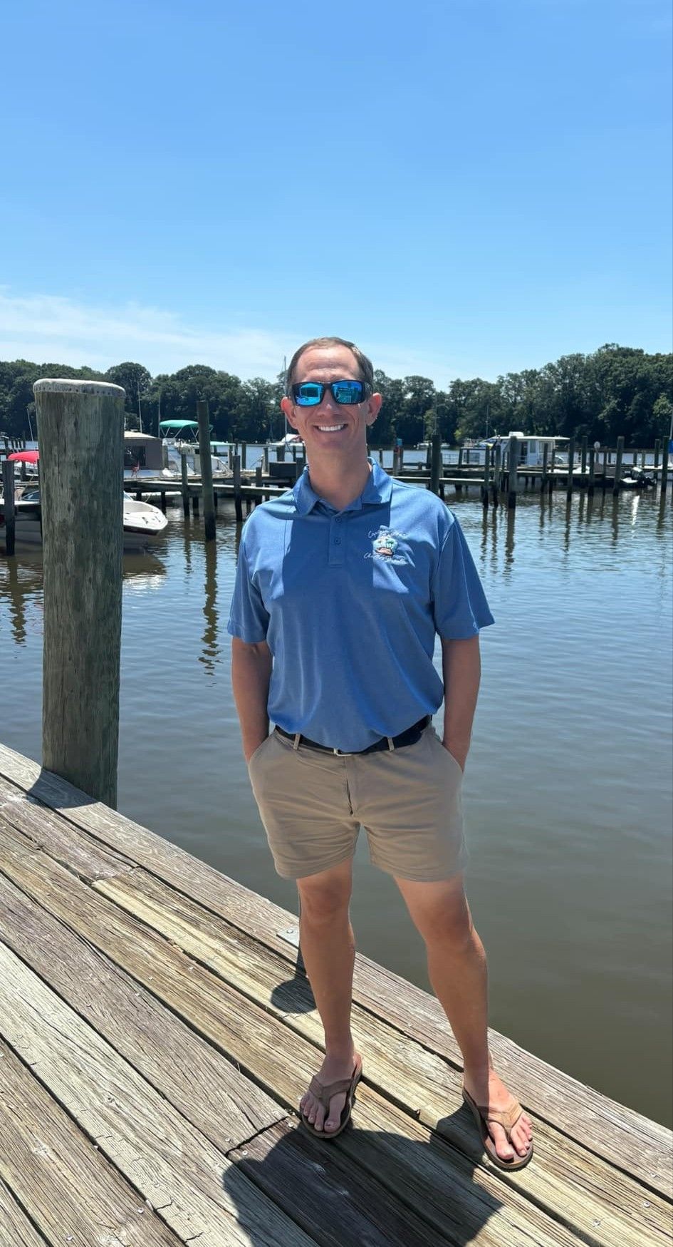 A man is standing on a dock next to a body of water.
